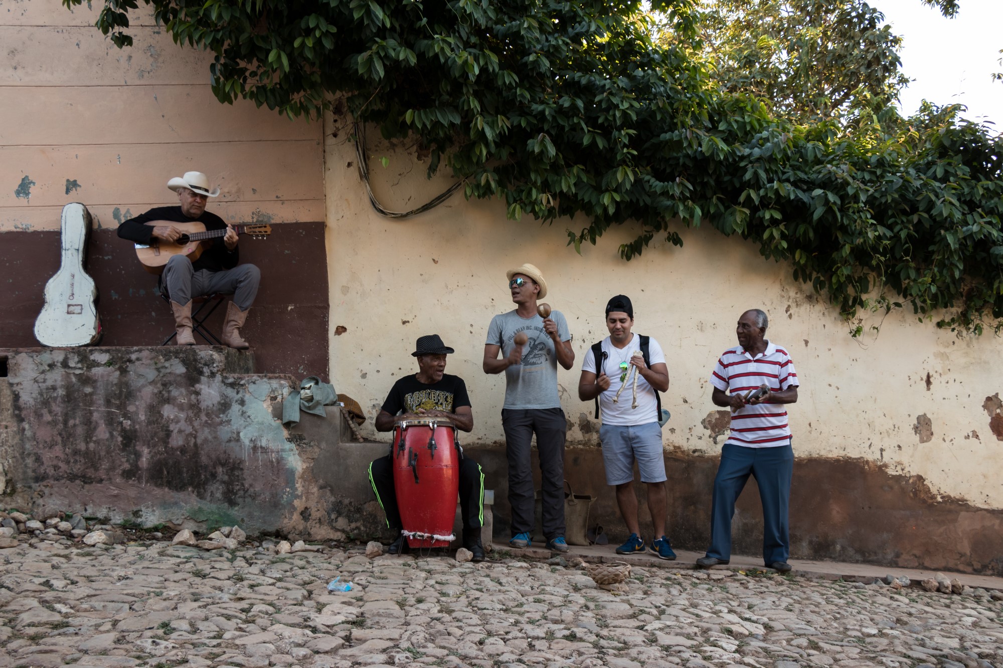 Men playing instruments at the side of a cobble-stoned street.
