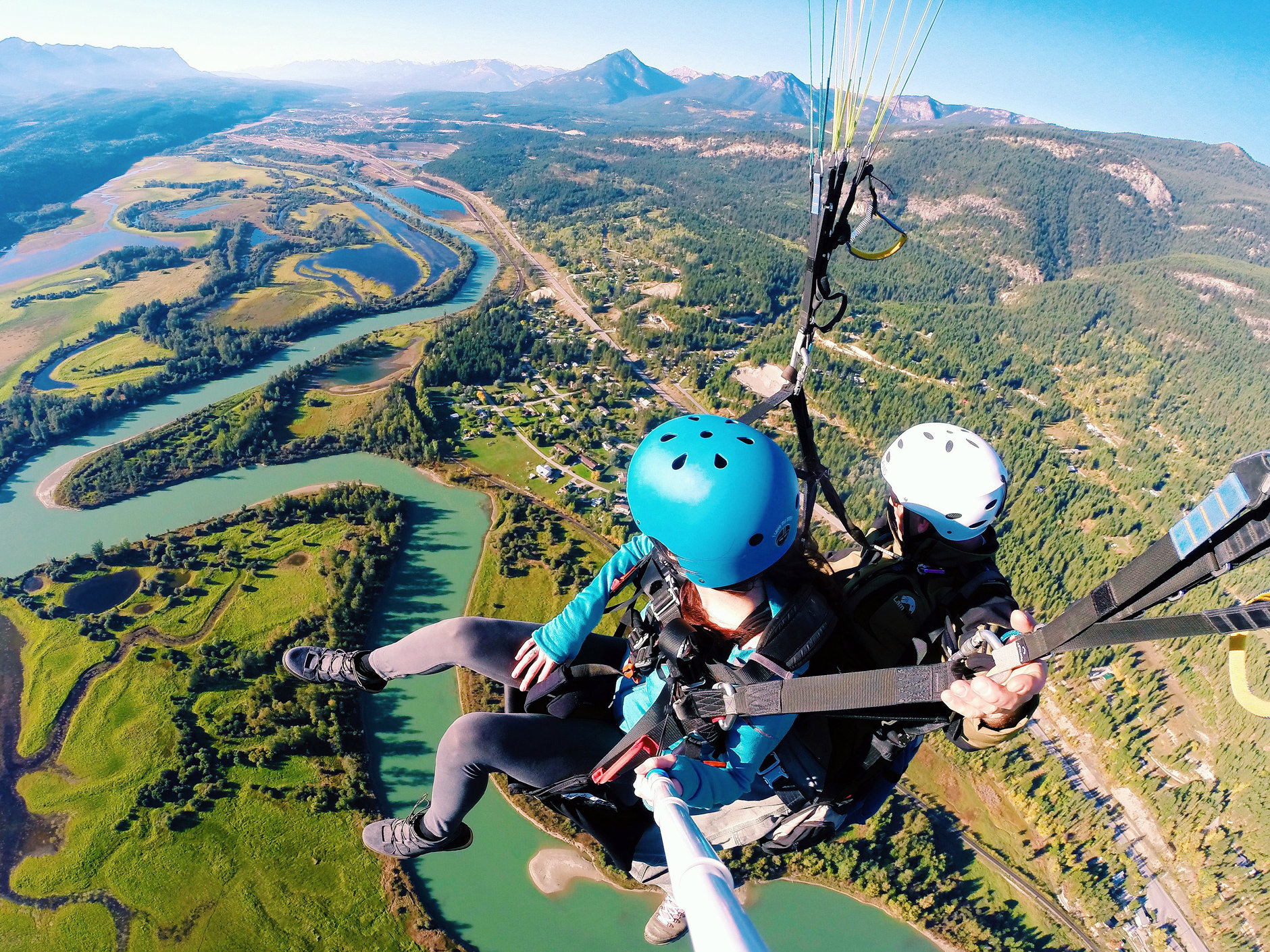 Two people paragliding over land and water landscapes.