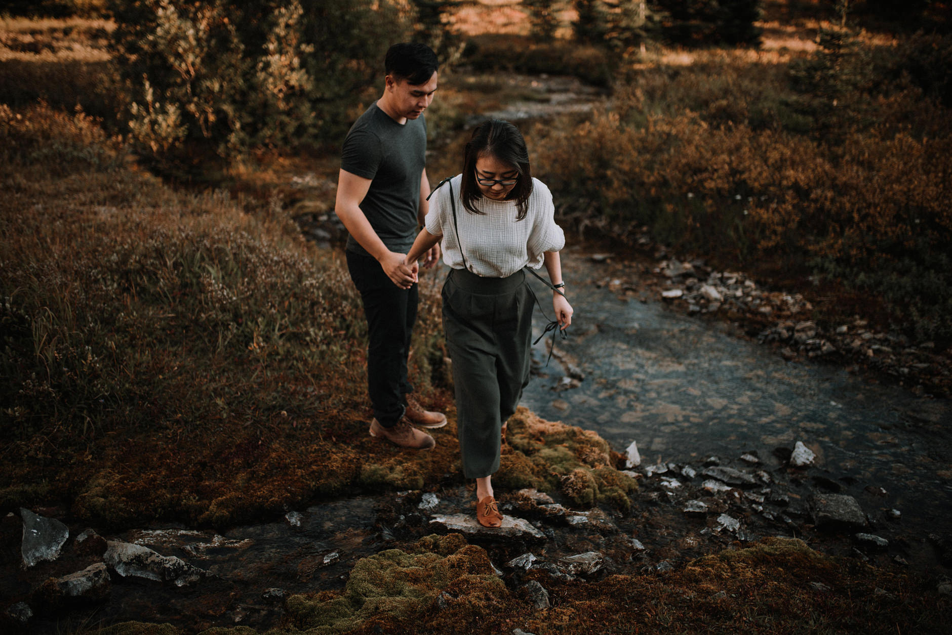A woman leading a man alongside a creek.