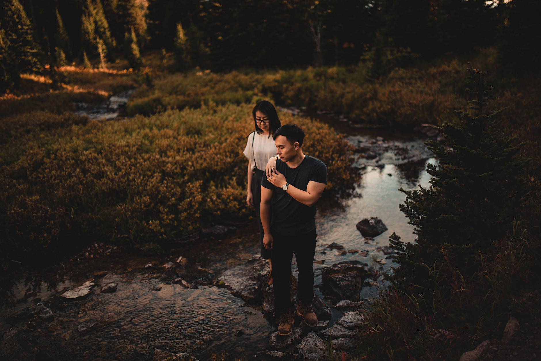 A man and woman standing on rocks in a creek.