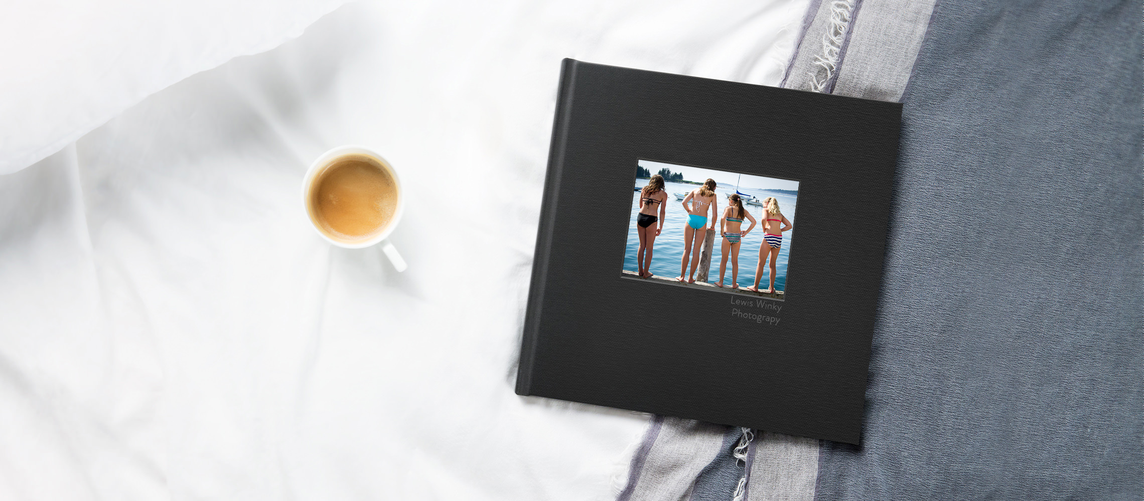 Schwarzes Hardcover-Fotobuch neben Kaffee auf Bett.