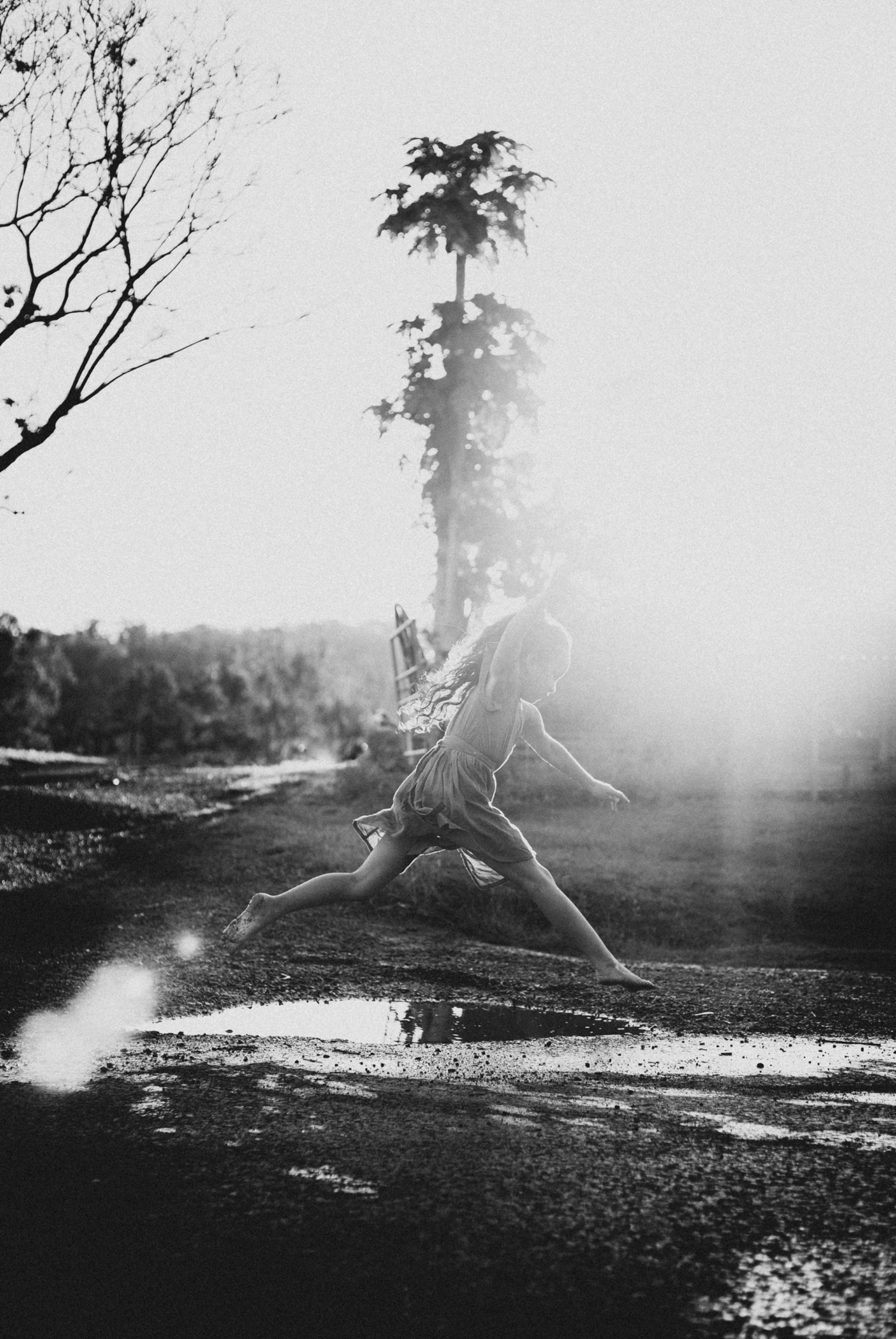 Girl jumping over a puddle of water.