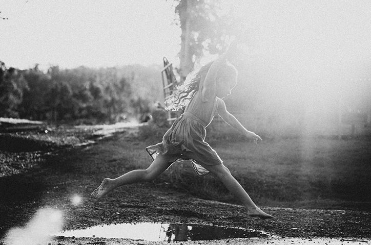 Girl jumping over puddle of water.