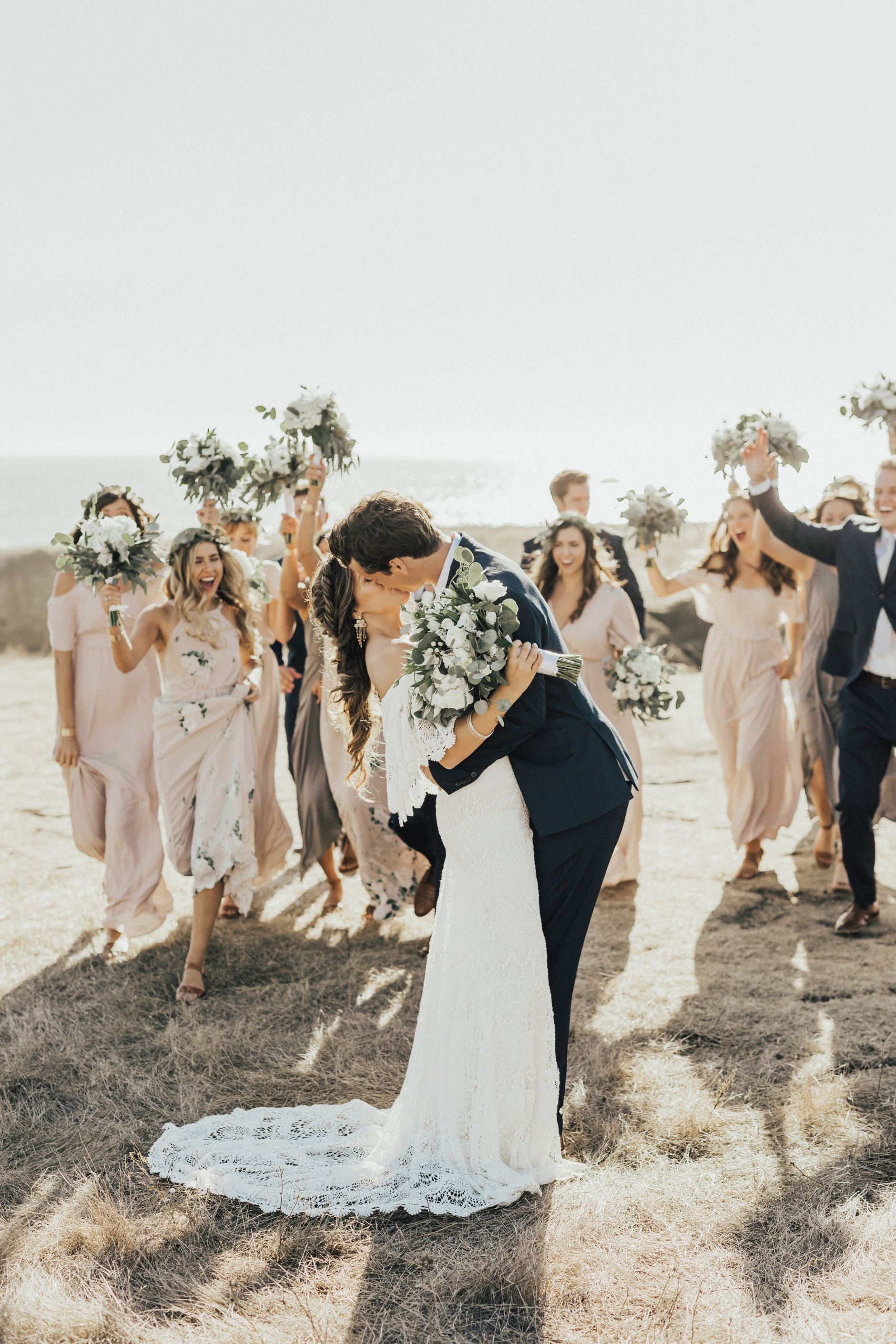 Bride and groom kissing, with their bridal party celebrating behind.
