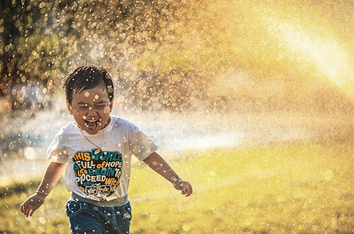 Child running through water sprinkler
