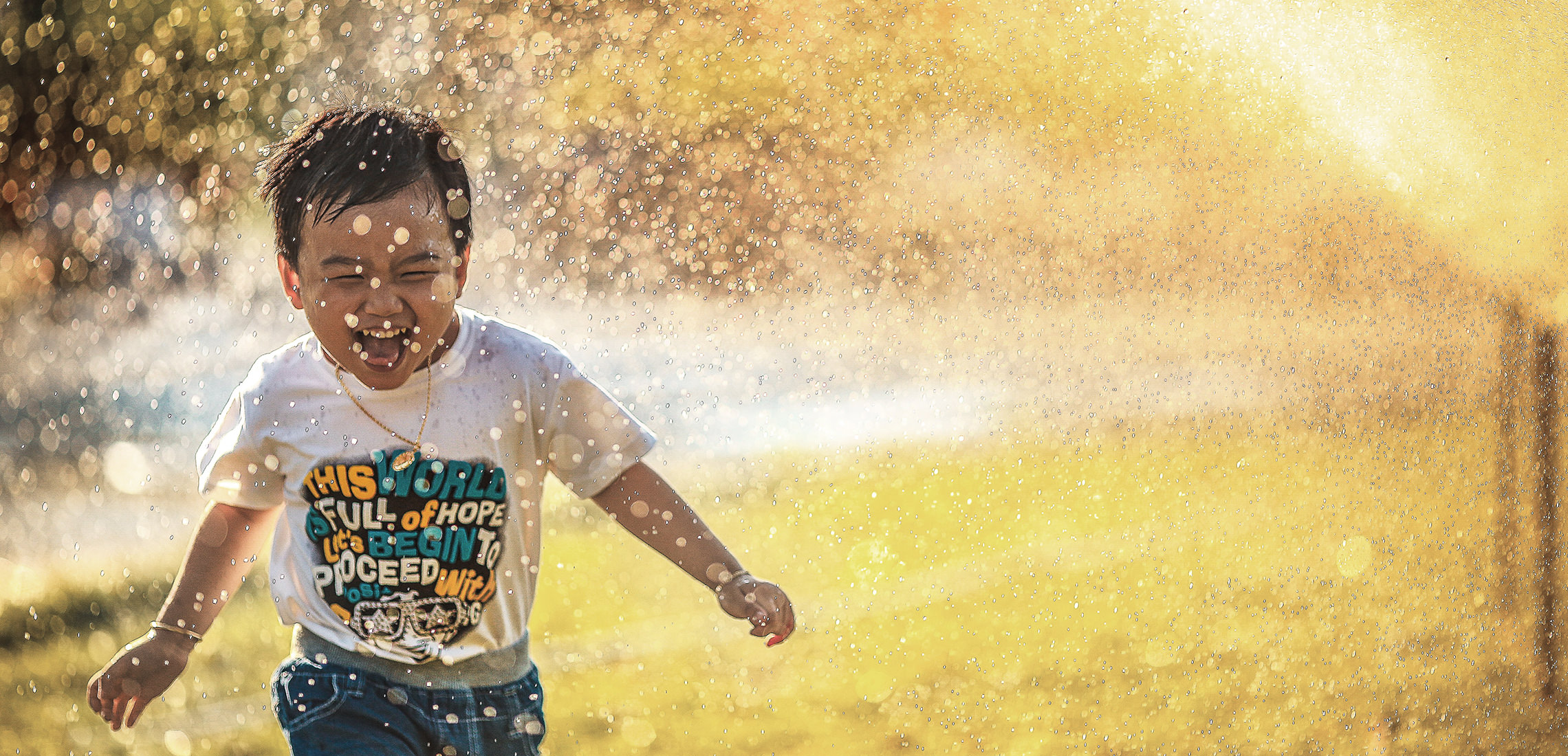 Young boy running through water sprinkler.
