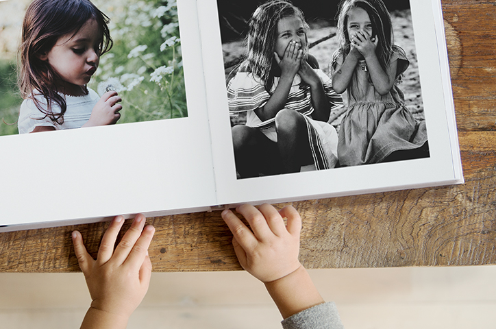 Un petit garçon feuilletant un livre de photos carré avec des photos de filles rieuses.