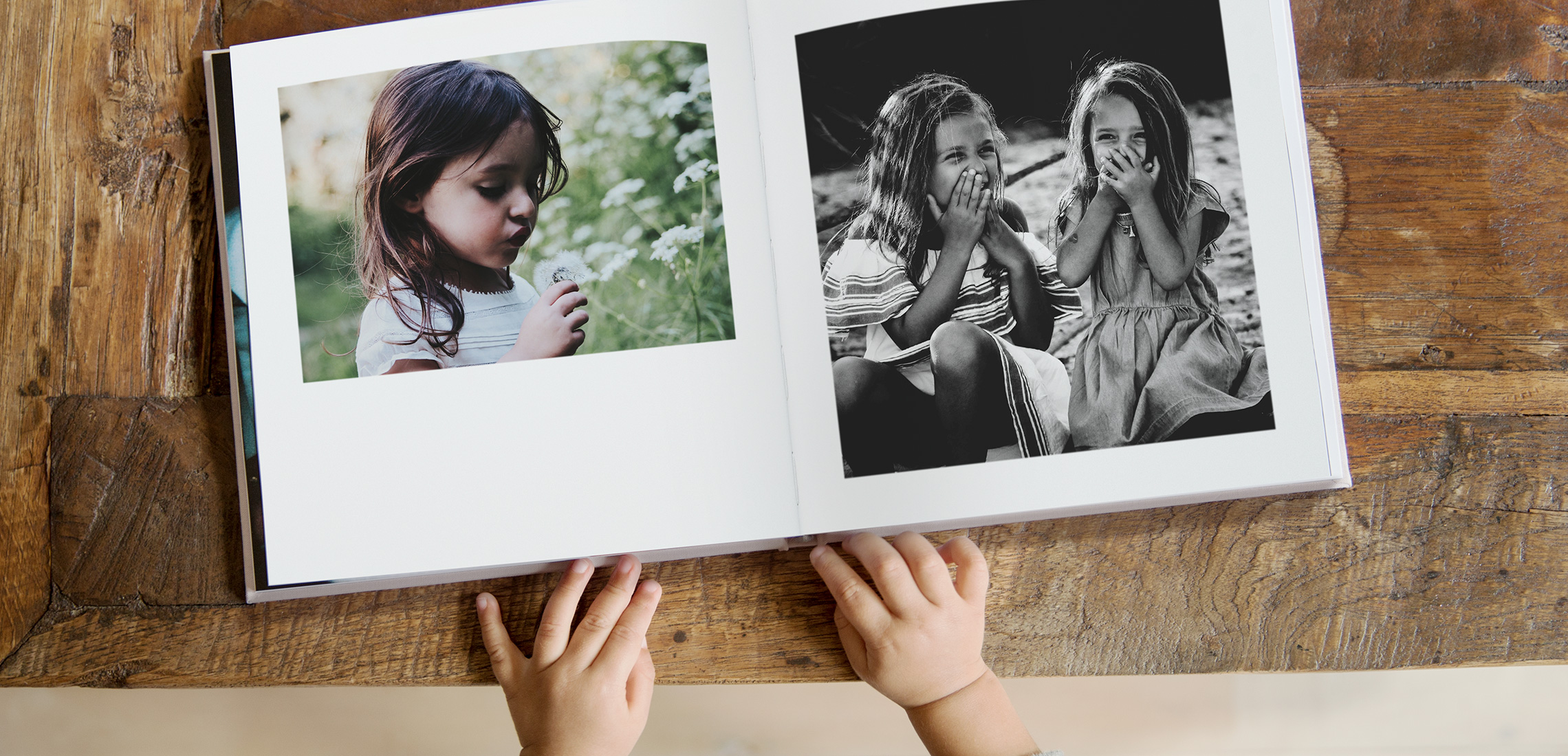 Un niño pequeño hojeando un fotolibro cuadrado con imágenes de niñas riendo.