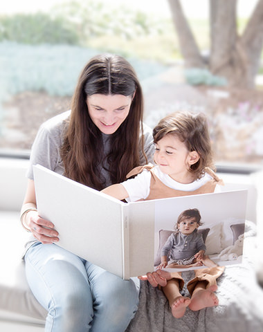 Menú desplegable de MILK Books, madre sentada con su hijo pequeño hojeando su álbum de fotos de bebé.