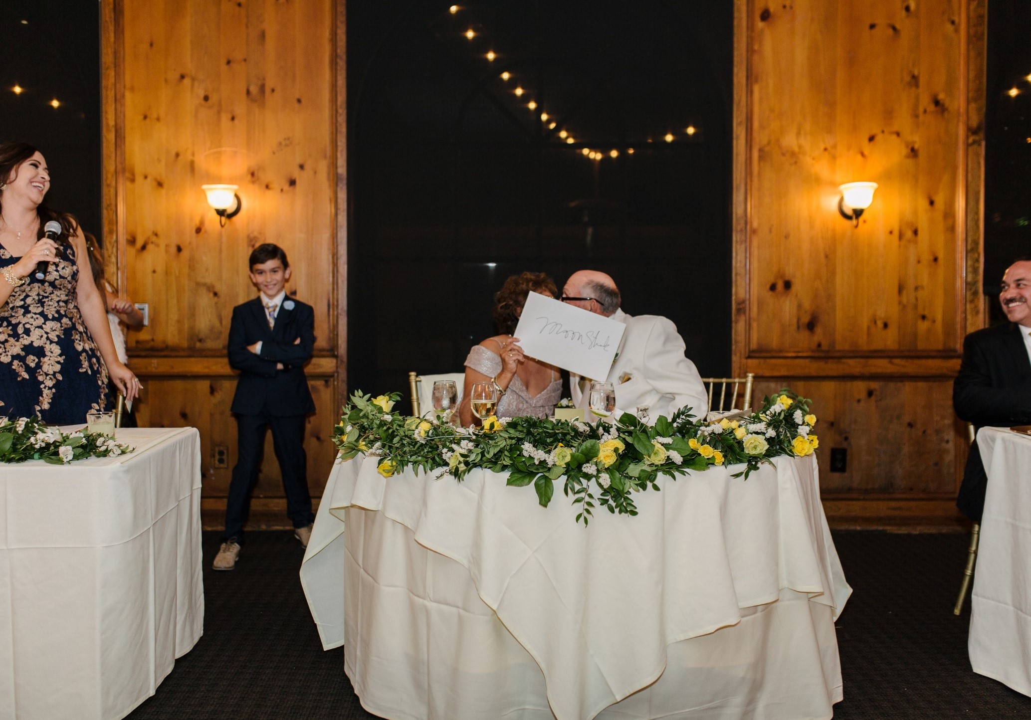 Couple at a table kissing behind a piece of paper.