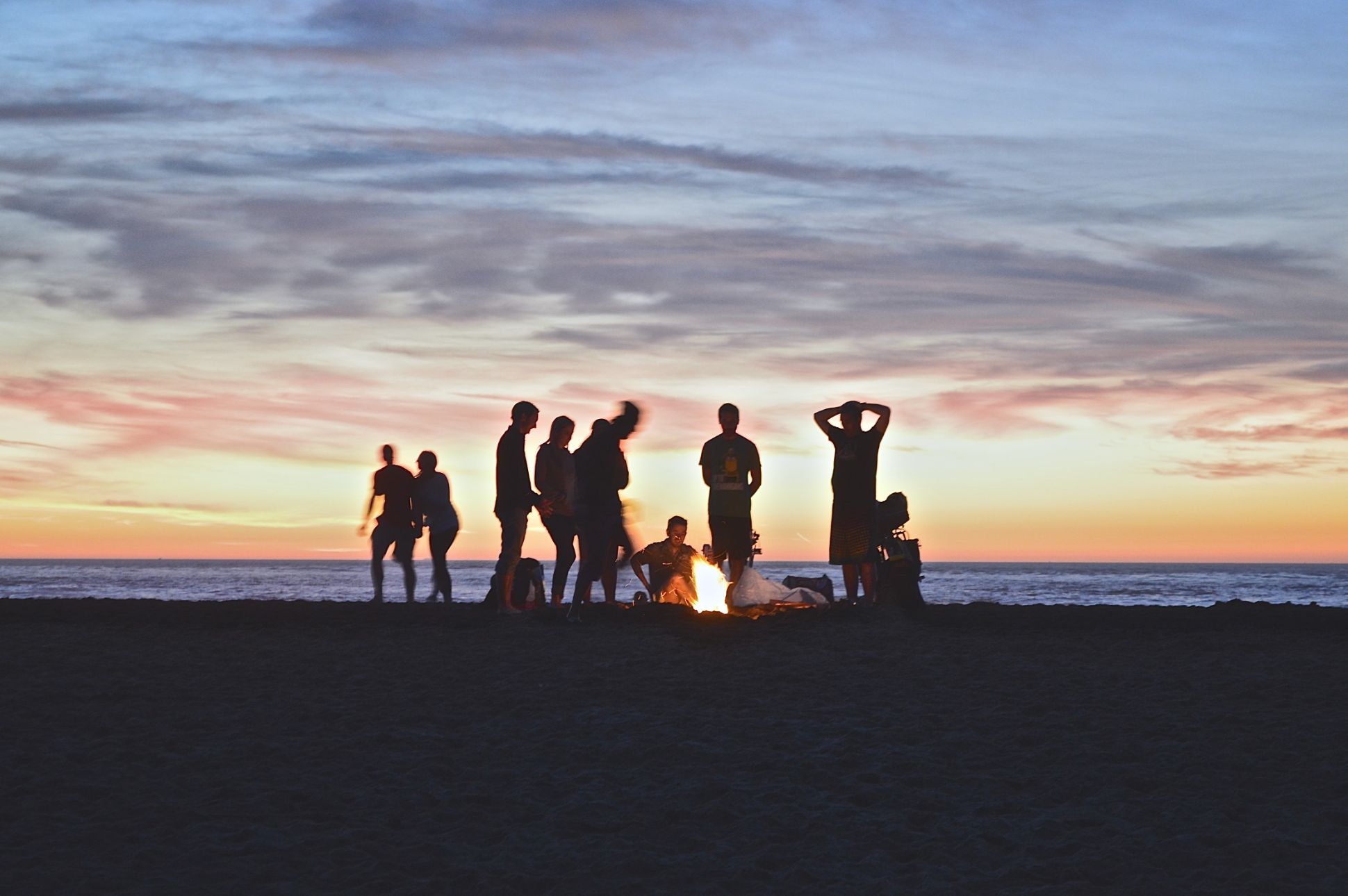 Group of people at the beach having a bonfire at sunset.