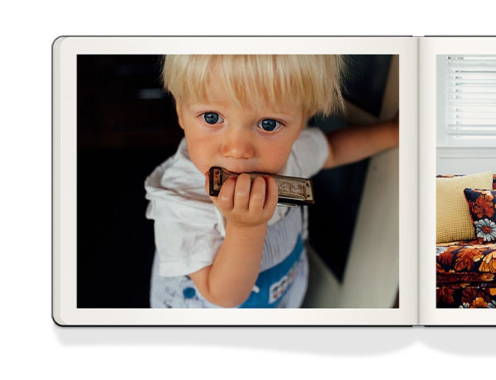 Open Moleskine photo book with image of a young boy playing a harmonica.