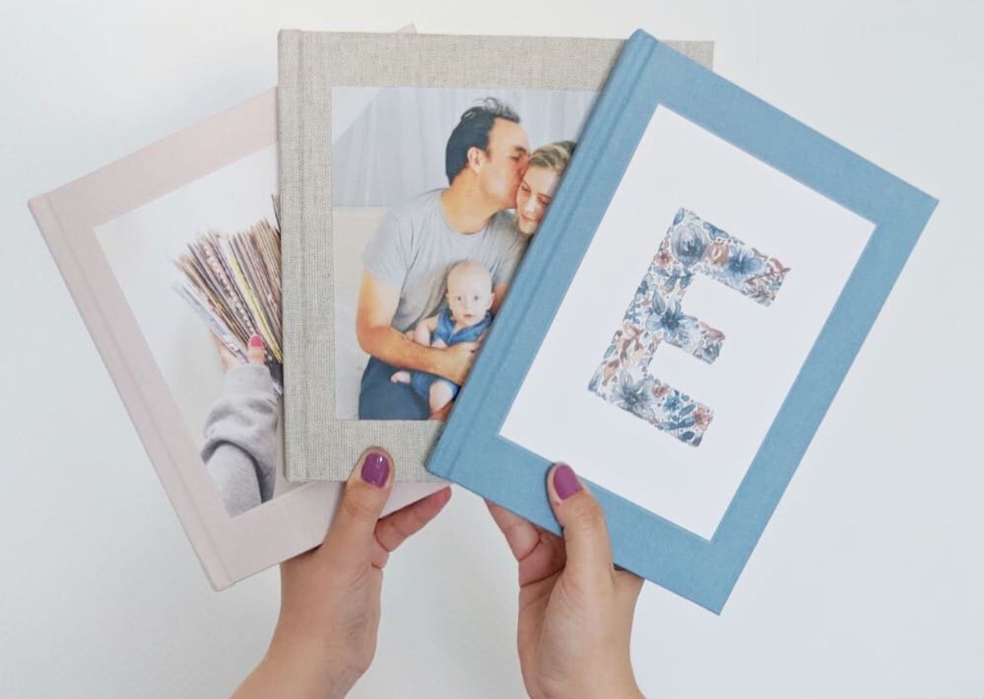 Hands holding three photo books in a fan shape.
