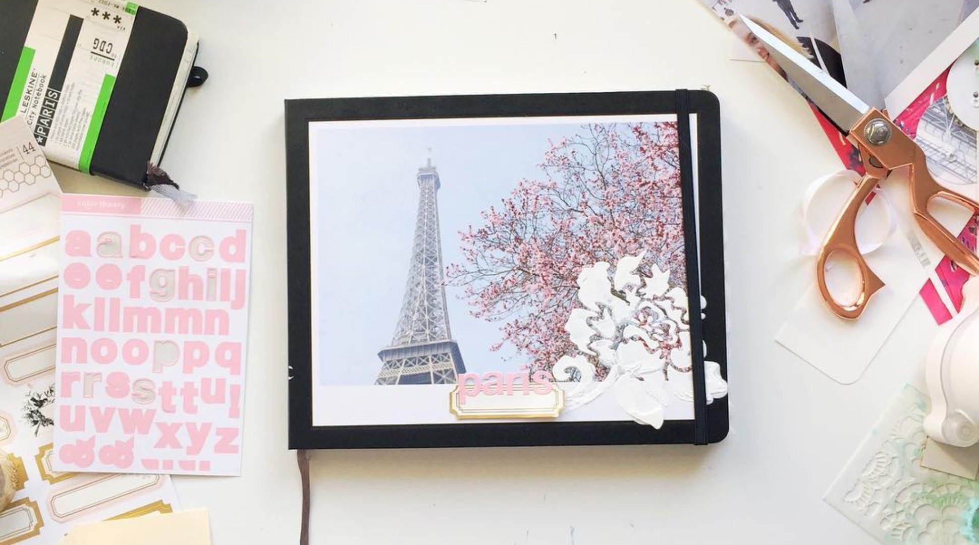 Flatlay of desk with scrapbooking accessories and a Moleskine Photo Book with a cover image of the Eiffel Tower.