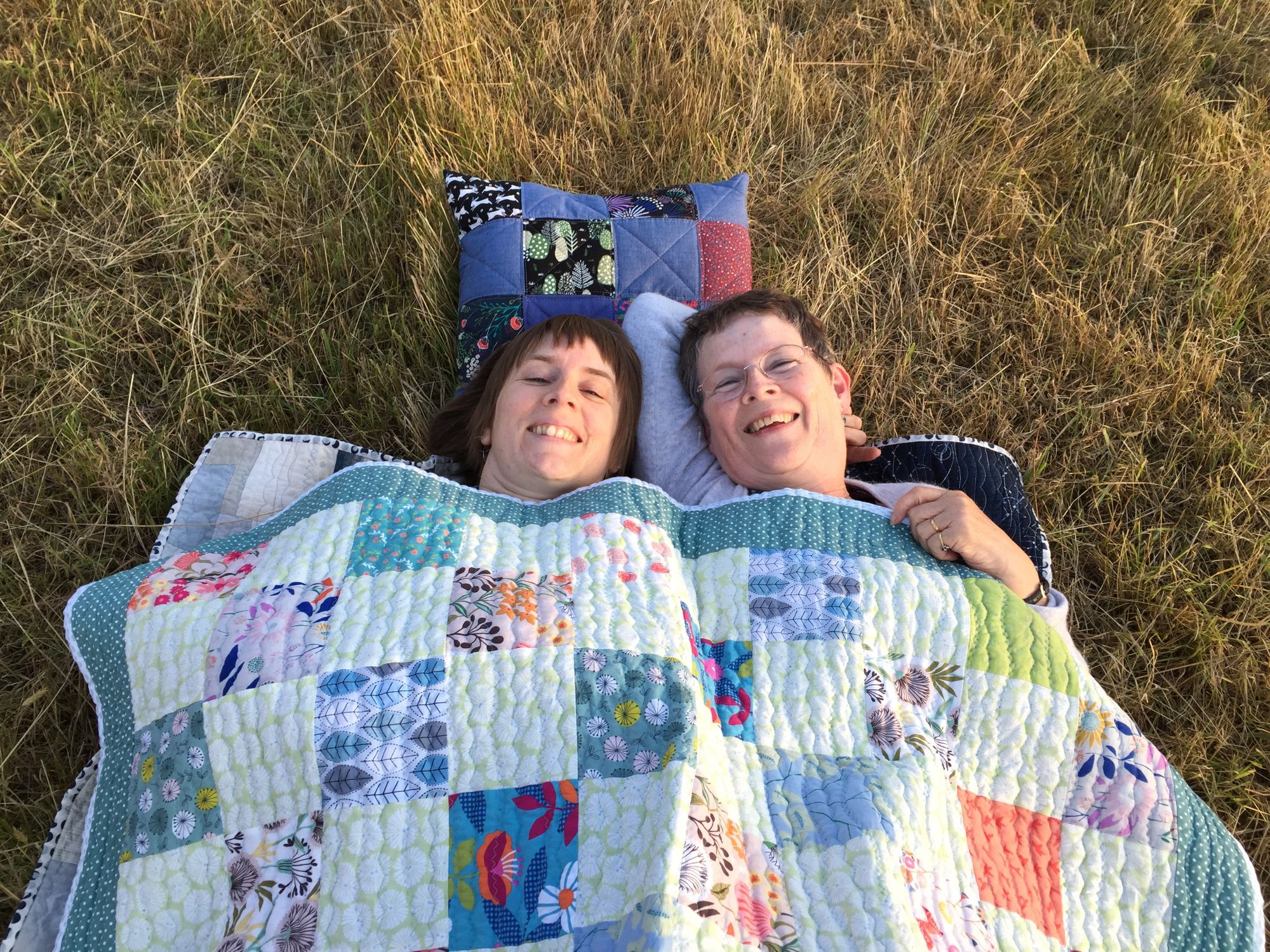 Woman and mother lying in grass under quilt