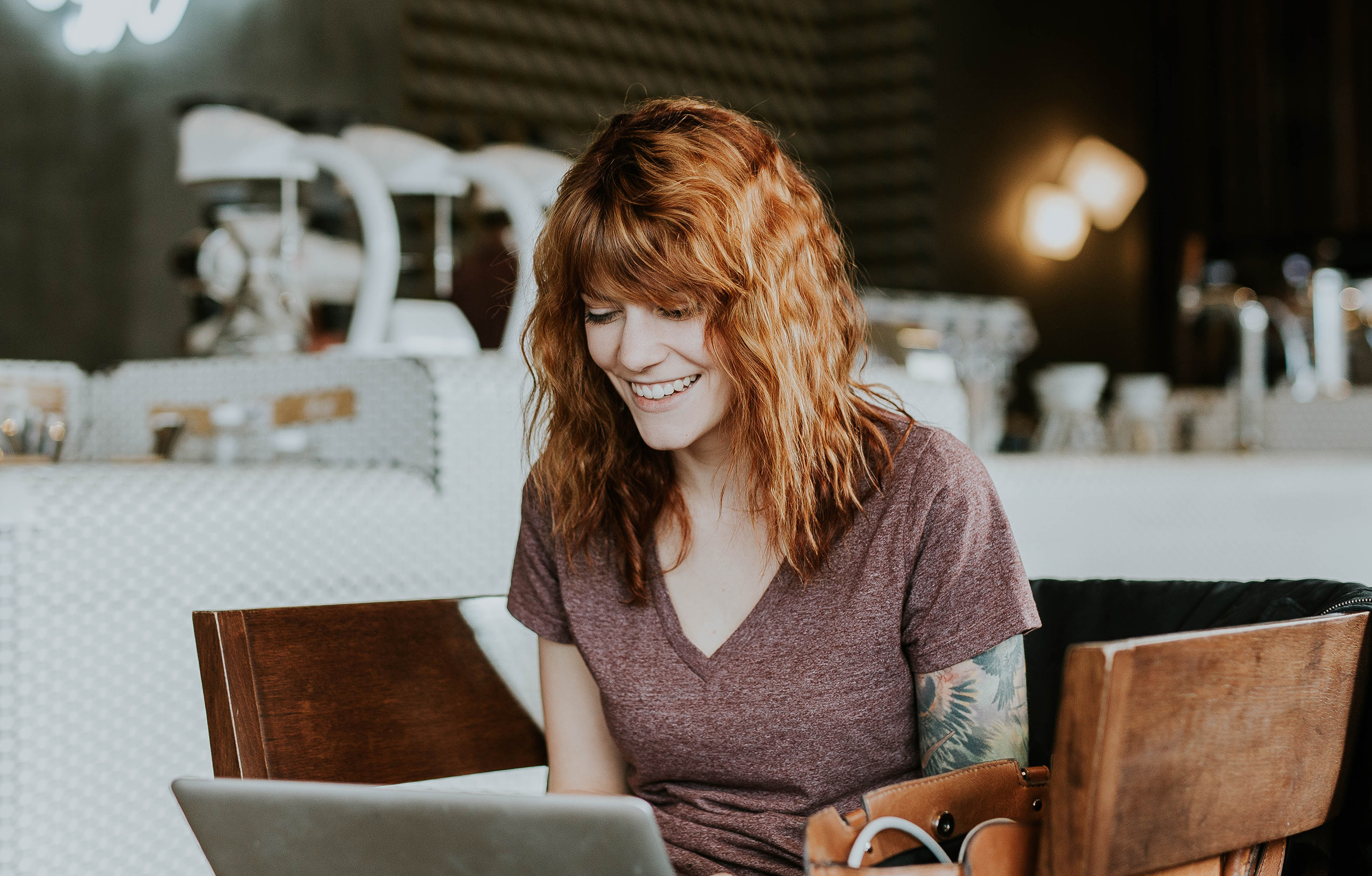 Mujer en una cafetería sonriendo a la pantalla de su portátil.
