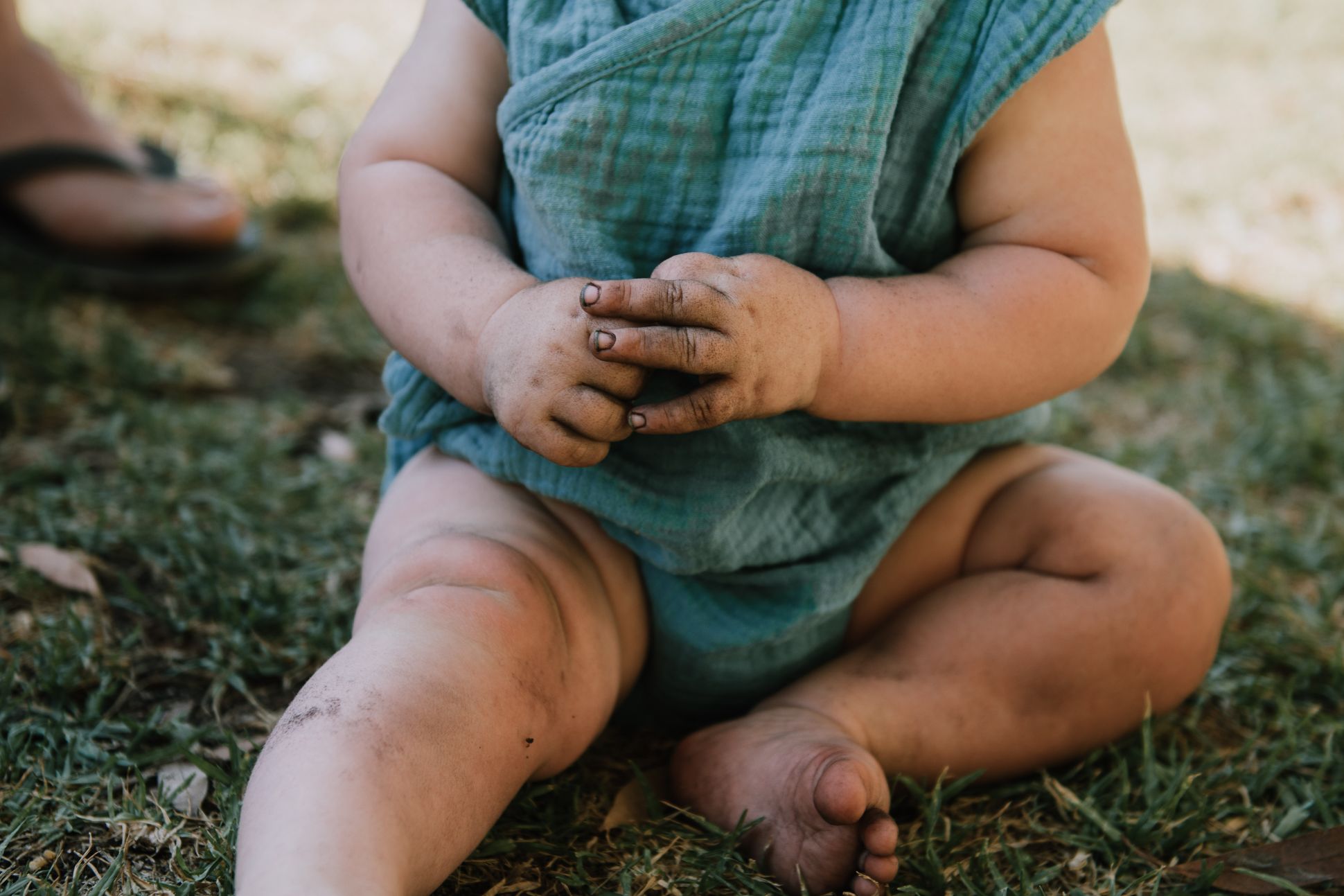 Young baby in a blue onesie playing in the garden.
