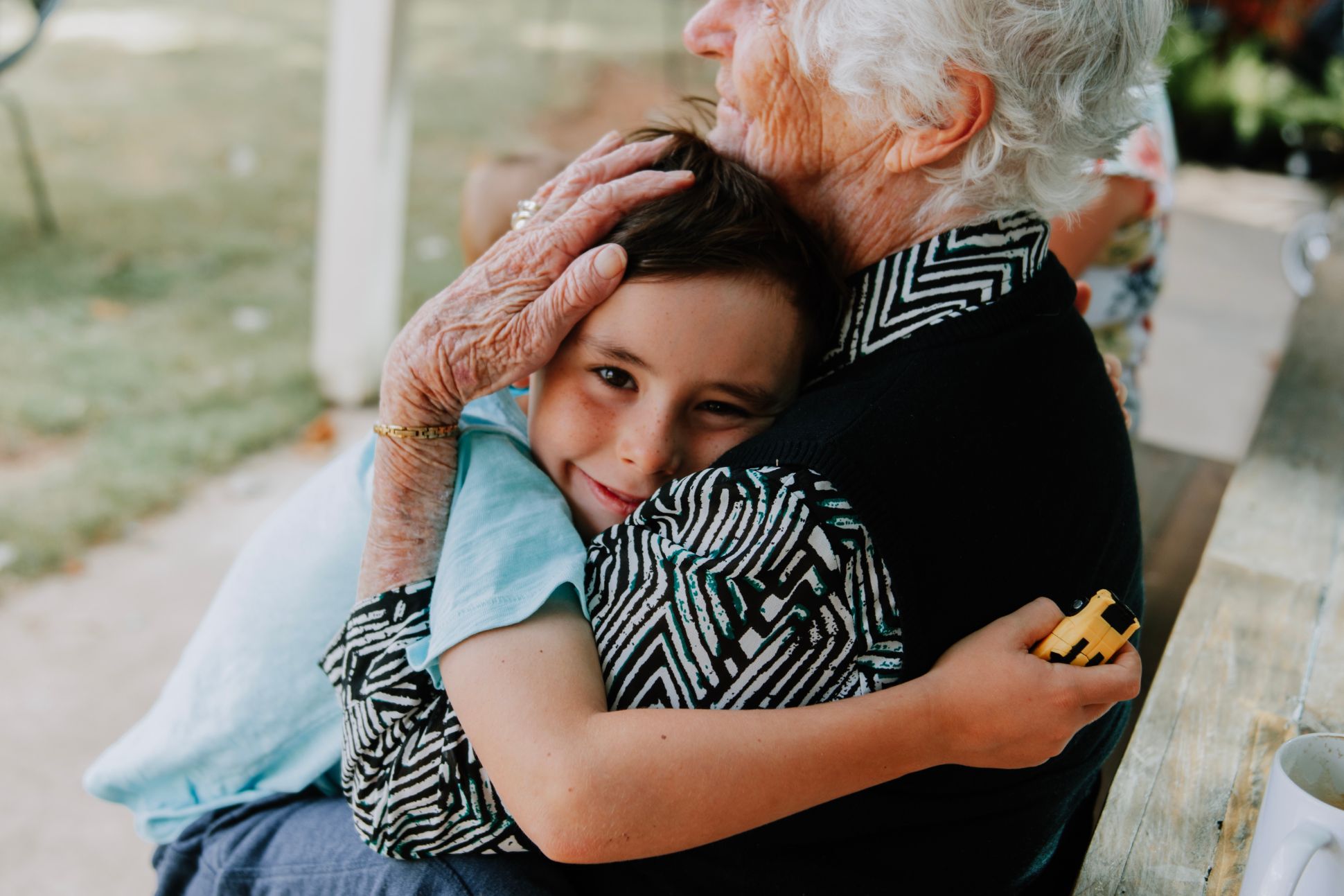 A young boy being embraced in a hug by and older woman.