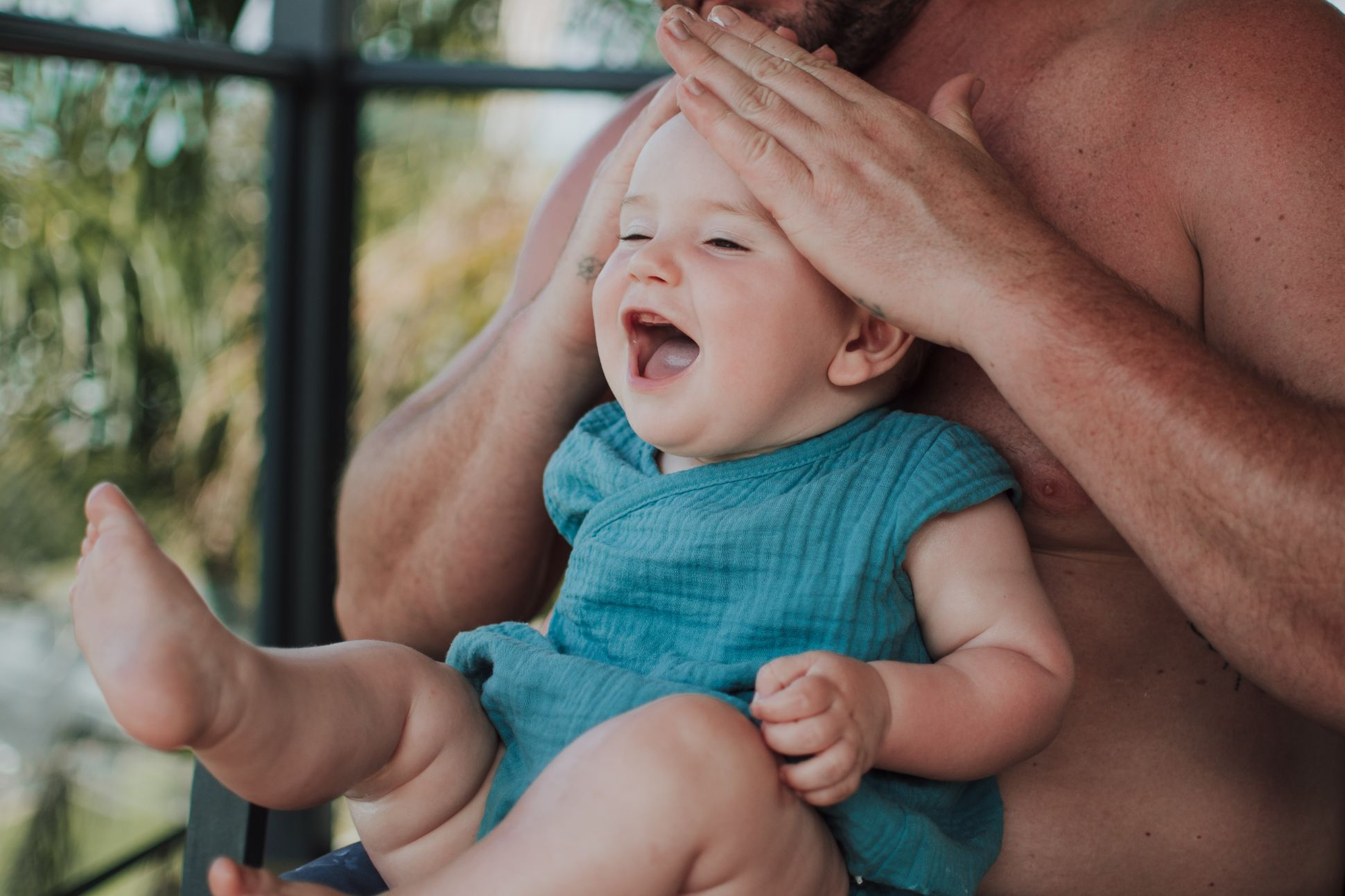 Baby in a blue onesie smiling, held by a male.