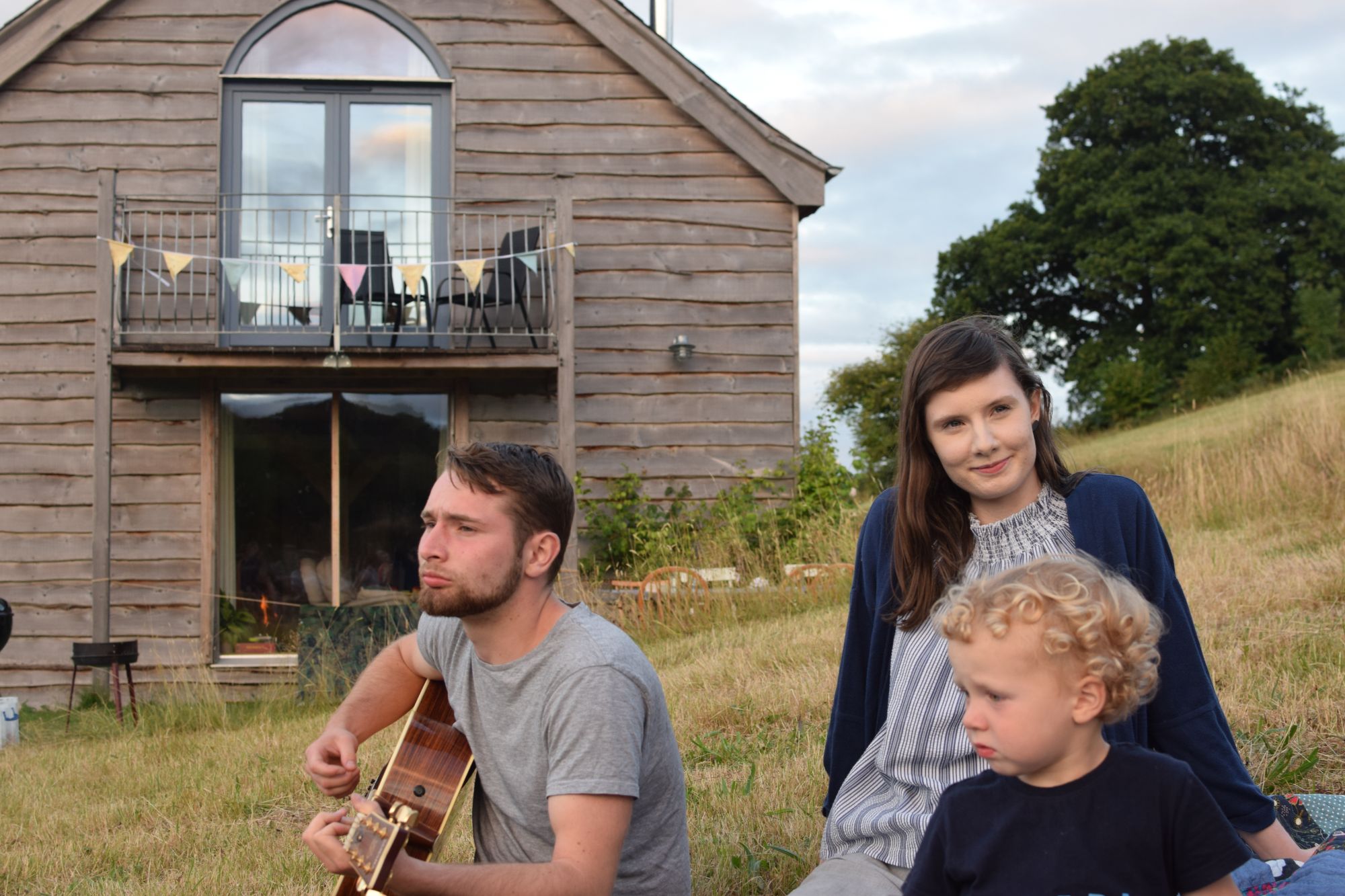 Man playing guitar on grass with woman and child
