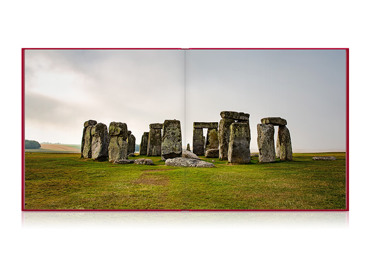 Quadratisches Reise-Fotobuch aufgeschlagen mit einem Foto des Steindekmales Stonehenge in England.