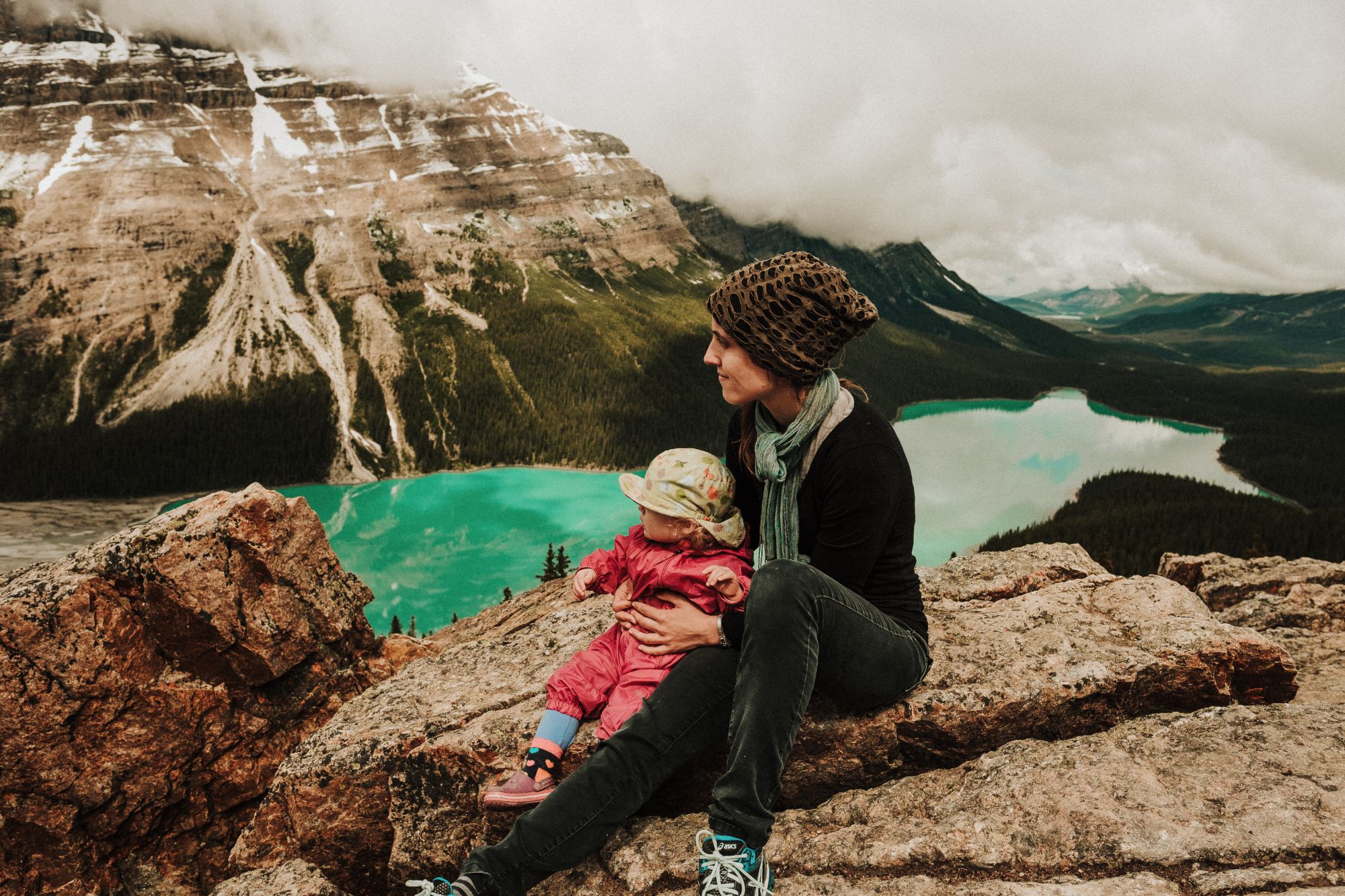 Woman and child atop a mountain overlooking a lake.