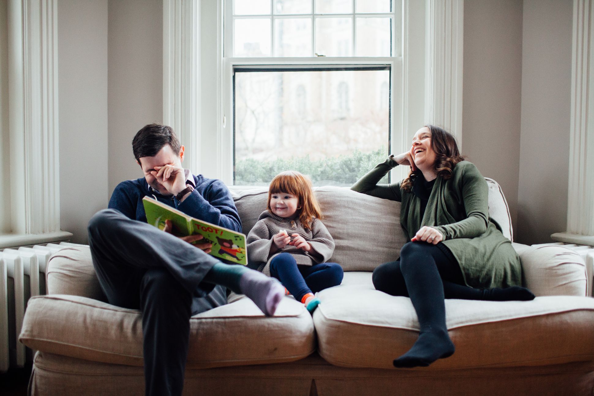 Family sitting on couch reading book together.