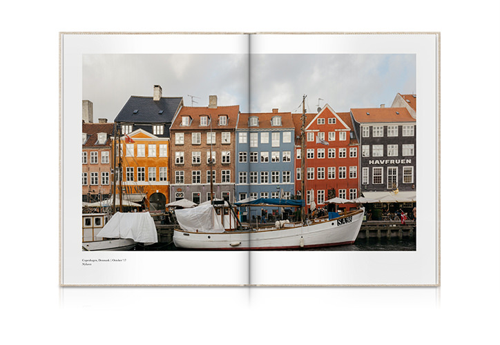 Aufgeschlagenes Reisefotobuch im Hochformat mit einem Foto von Cafés und Restaurants an der Uferpromenade in Kopenhagen.
