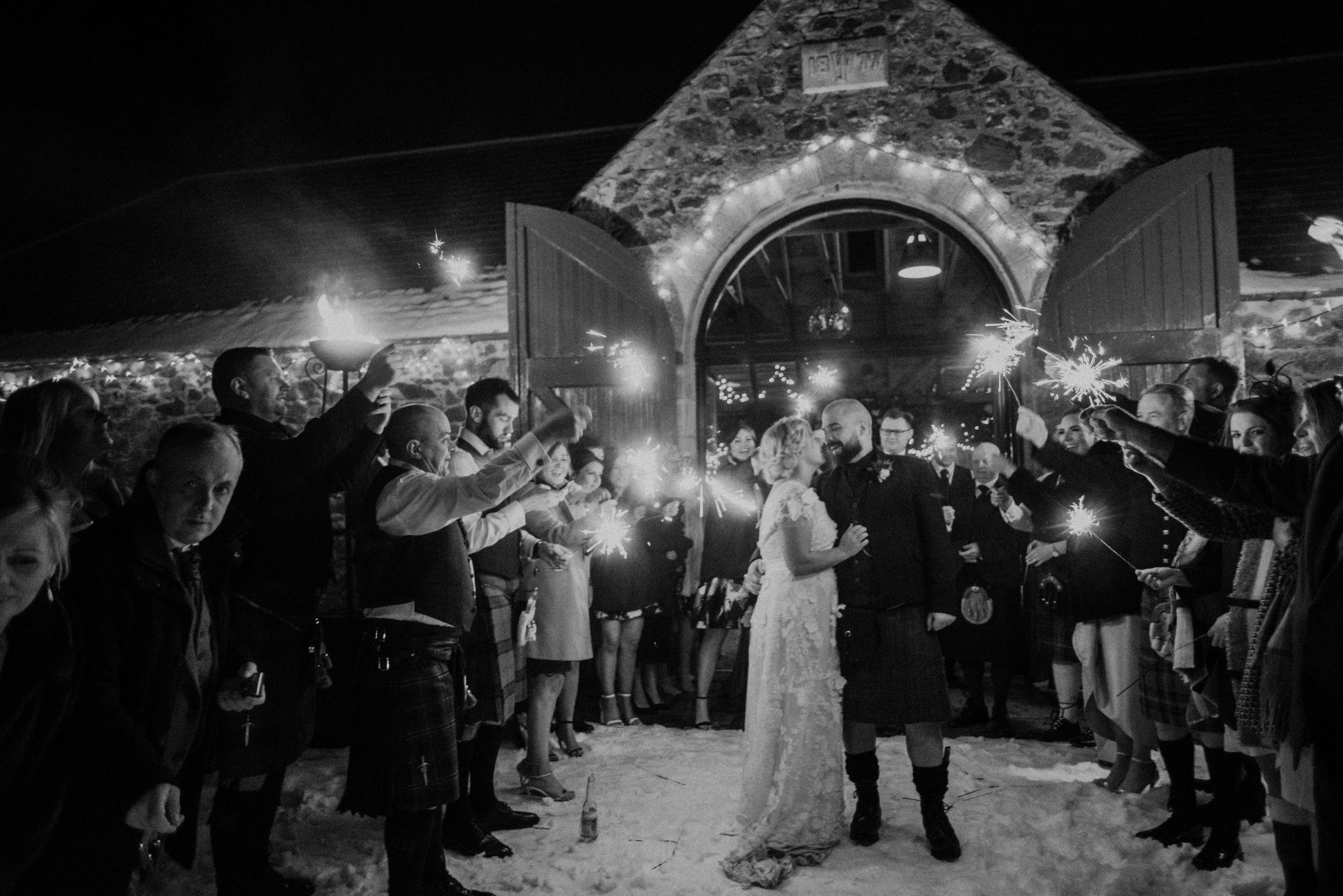 Bride and groom kiss as wedding guests hold sparklers