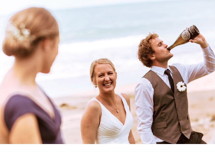 Groom drinking wine as bride smiles at bridesmaid