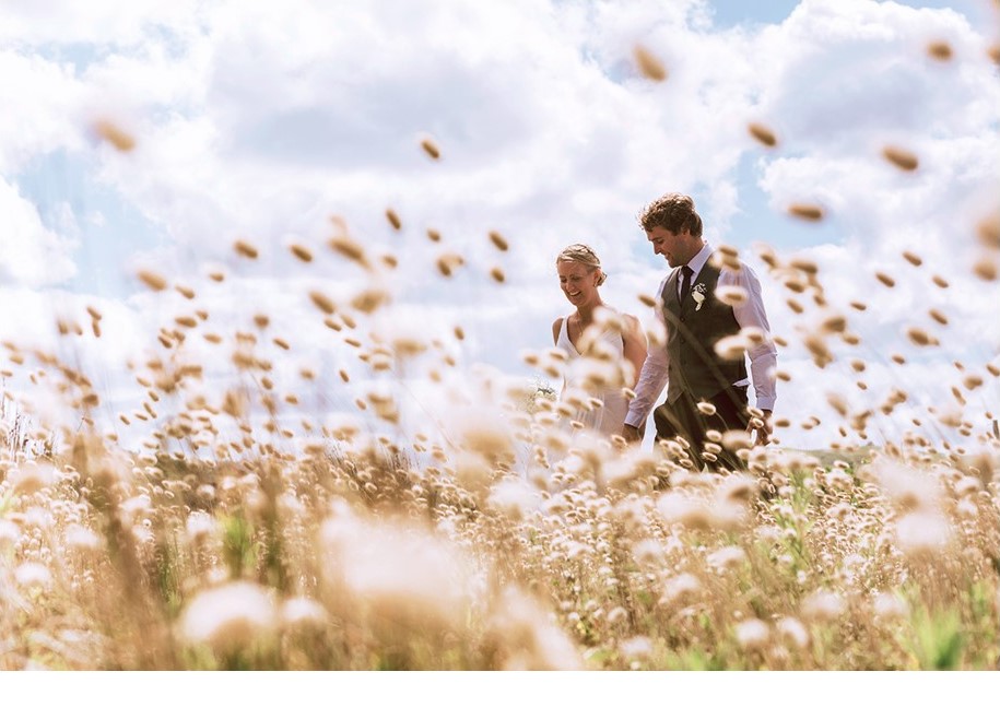 Bride and groom hold hands as they walk through field