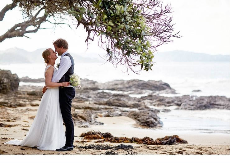 Bride and groom embrace on beach