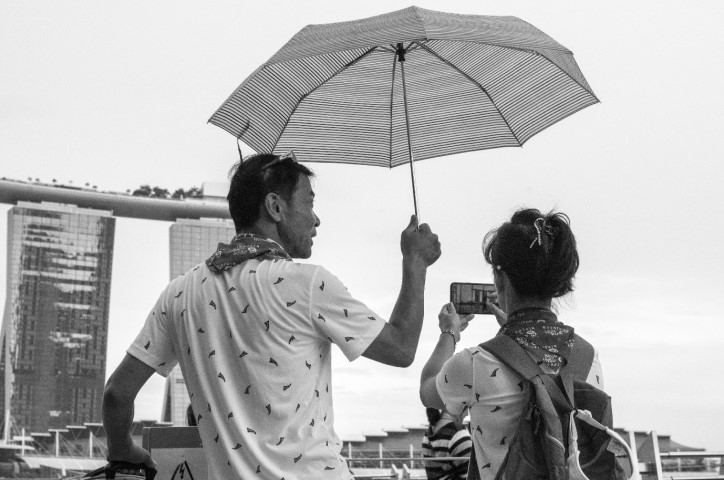 Man holding umbrella above himself and woman taking photo