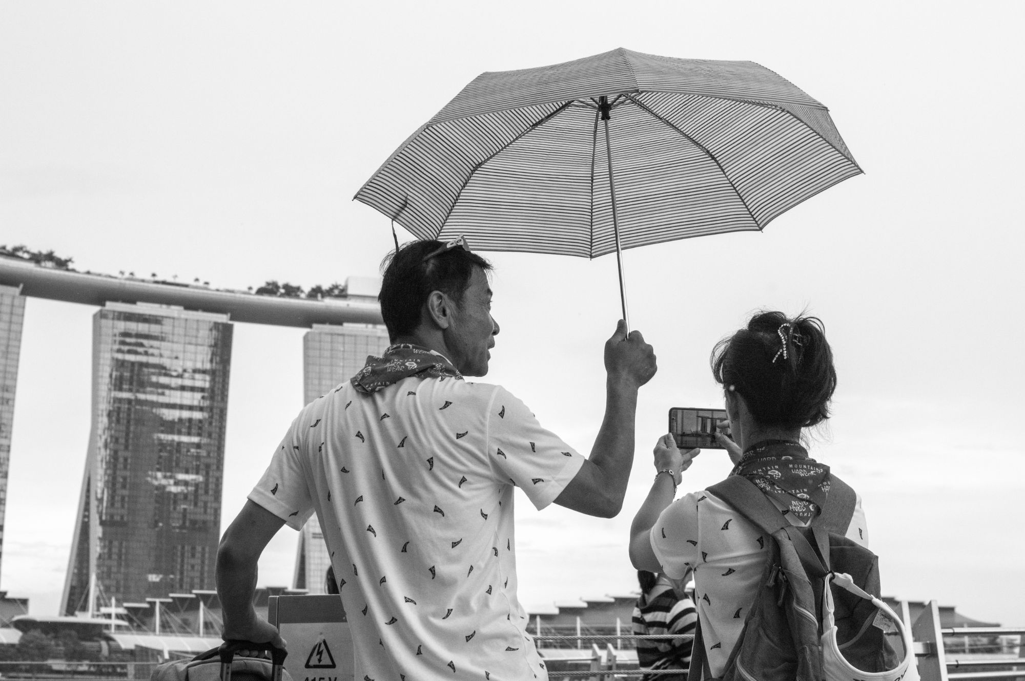 Man holding umbrella above himself and woman taking photo