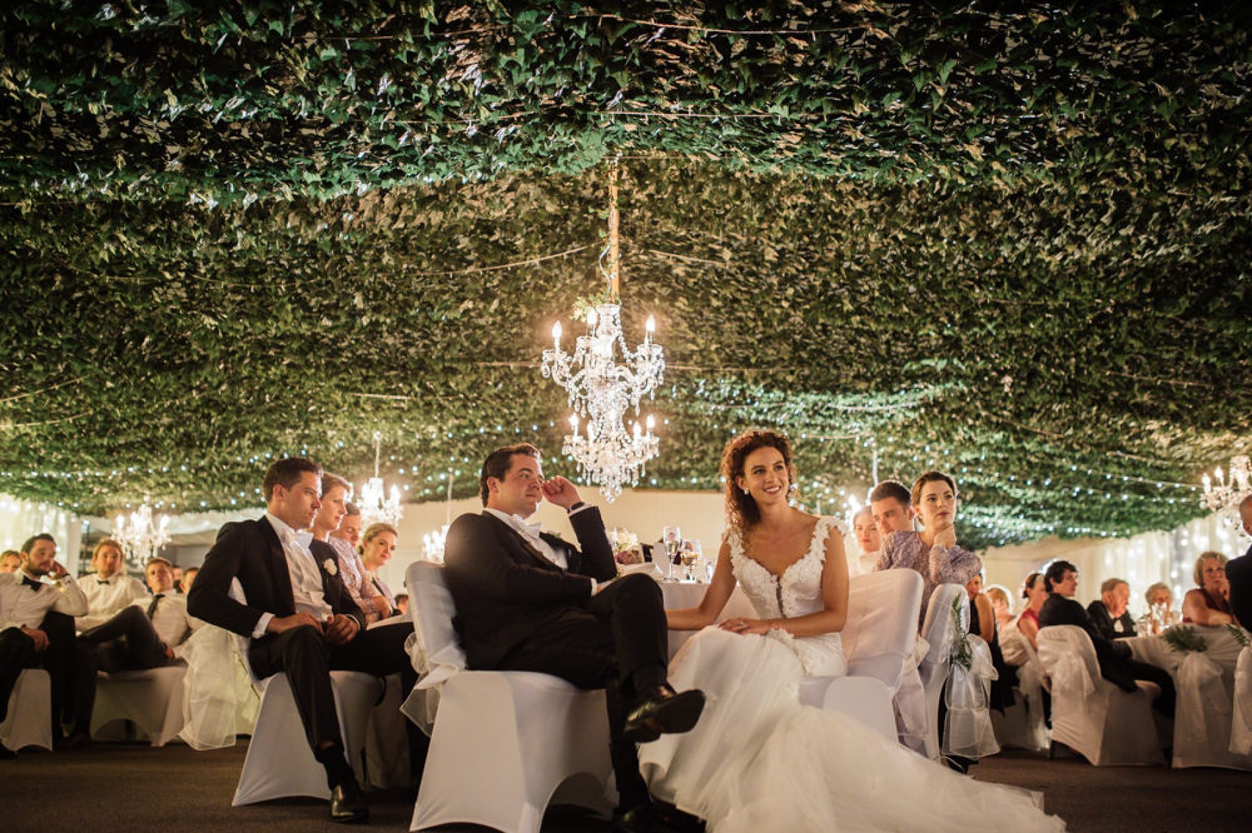 Wedding reception with couple and guests in chandelier lit hall.