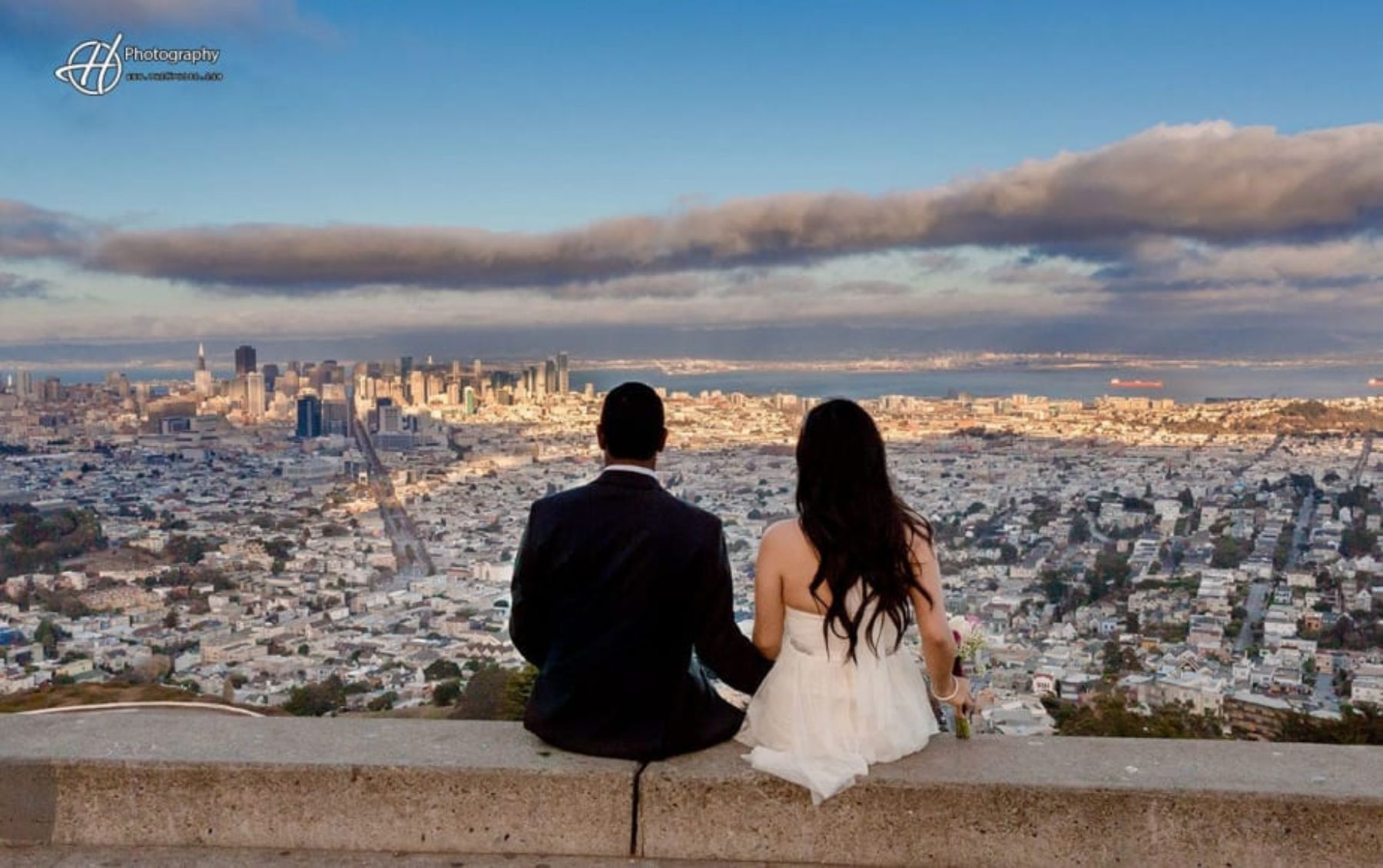 Bride and groom sitting backs to camera looking at city