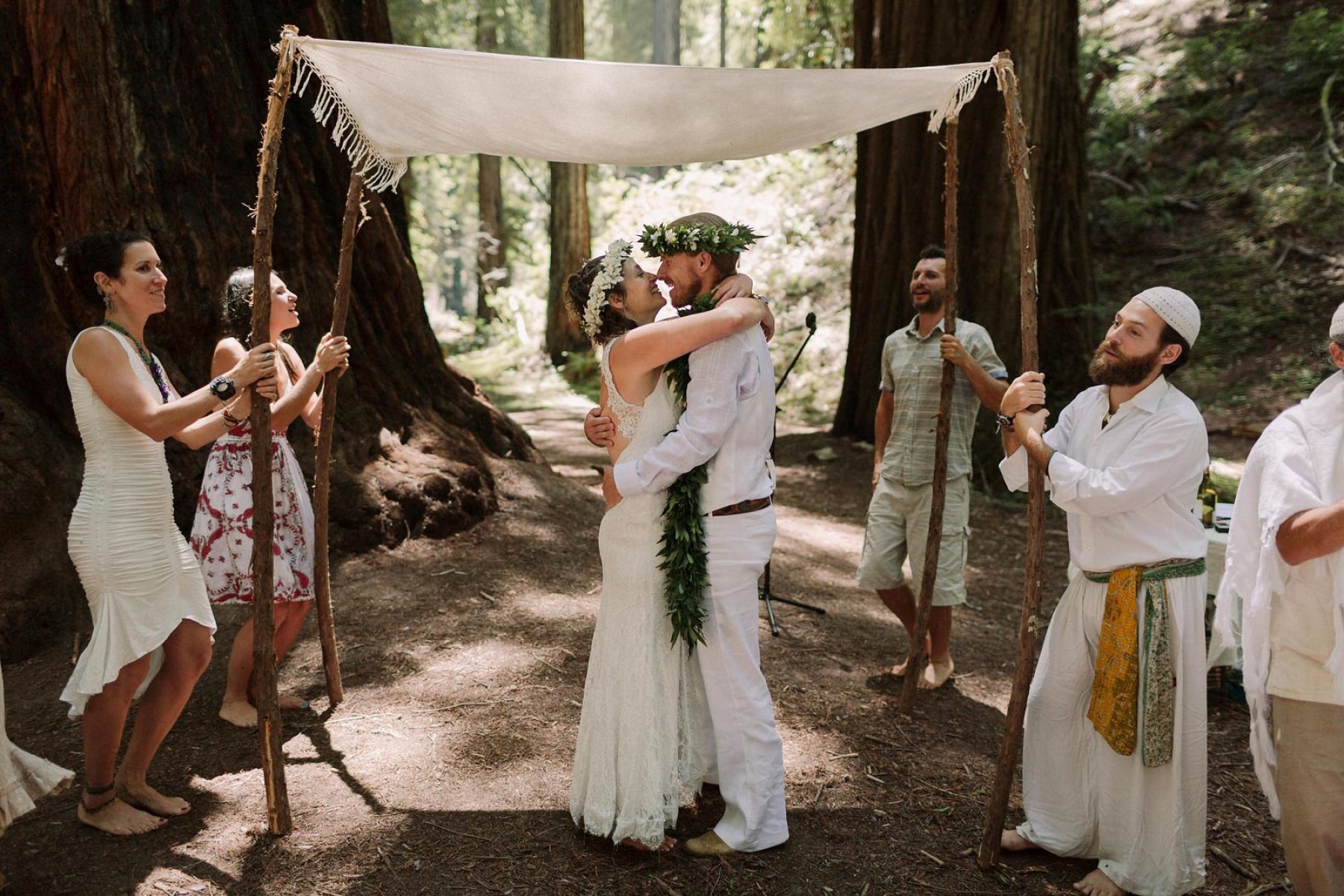 Bride and groom in all white being married barefoot in forest