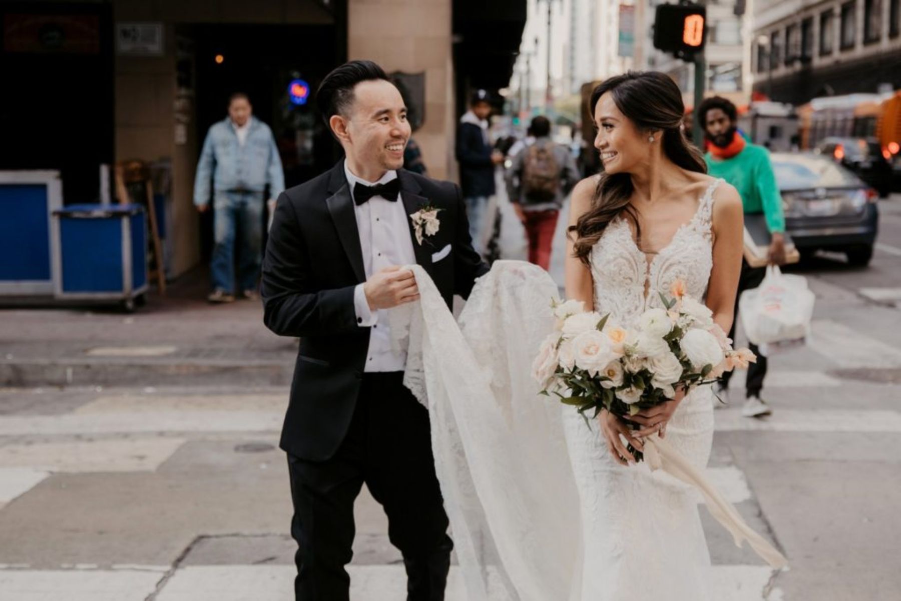 Groom holding bride's wedding dress train as they cross street