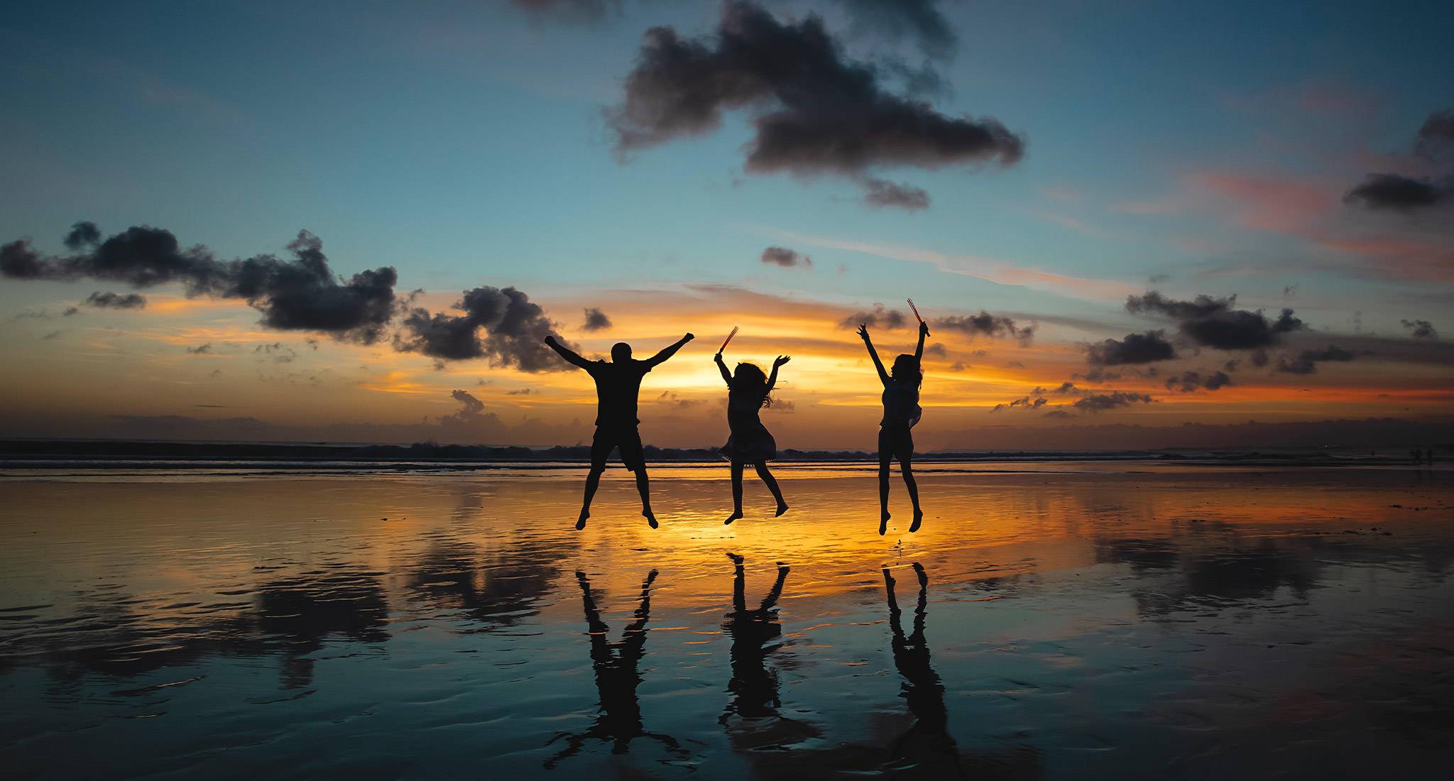 Silhouette von drei Menschen springend in der Luft am Strand während des Sonnenuntergangs.