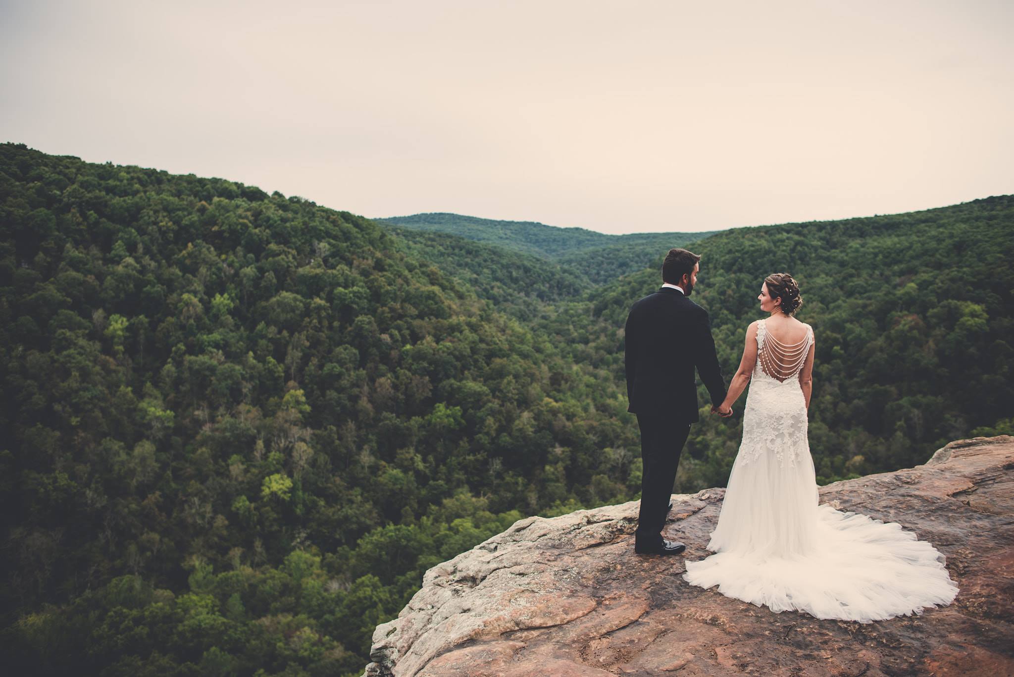 Newlyweds holding hands on a cliff edge.