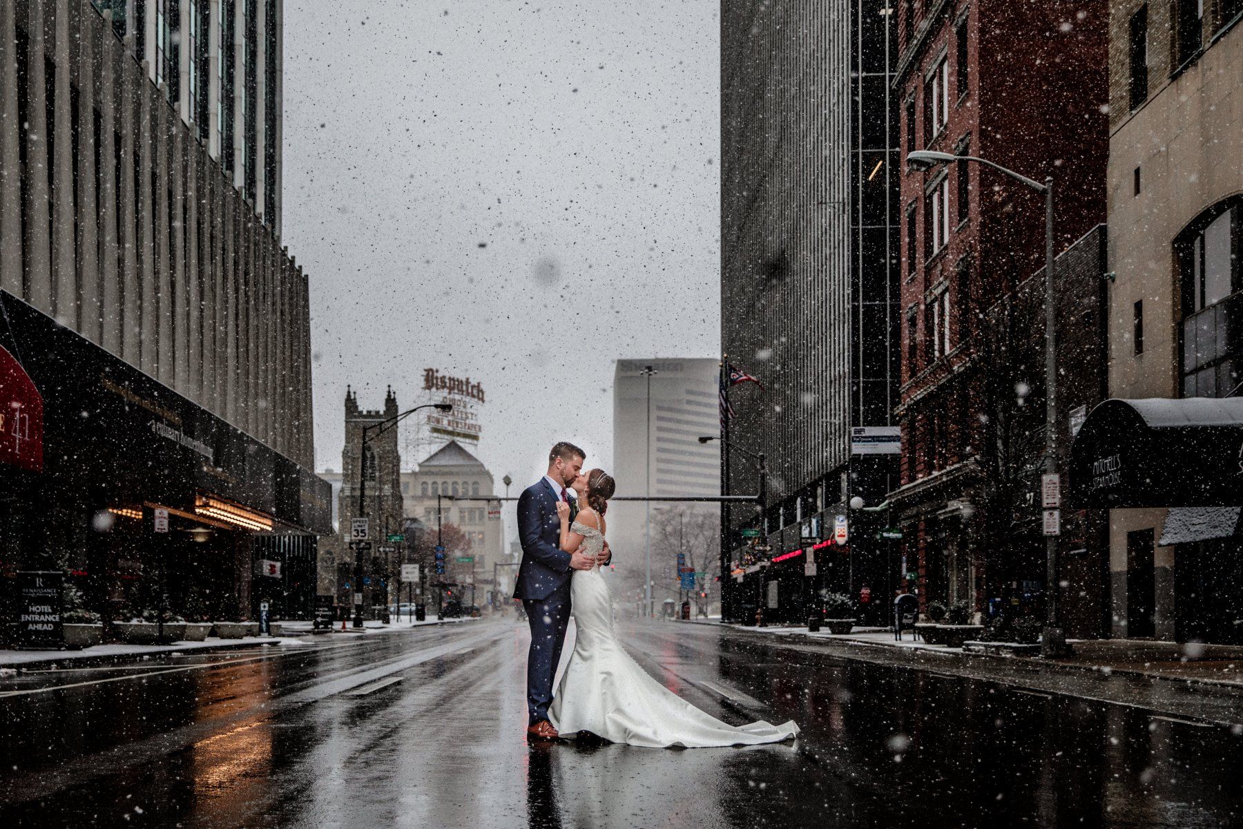 Newlywed couple kissing in the street while snow falls