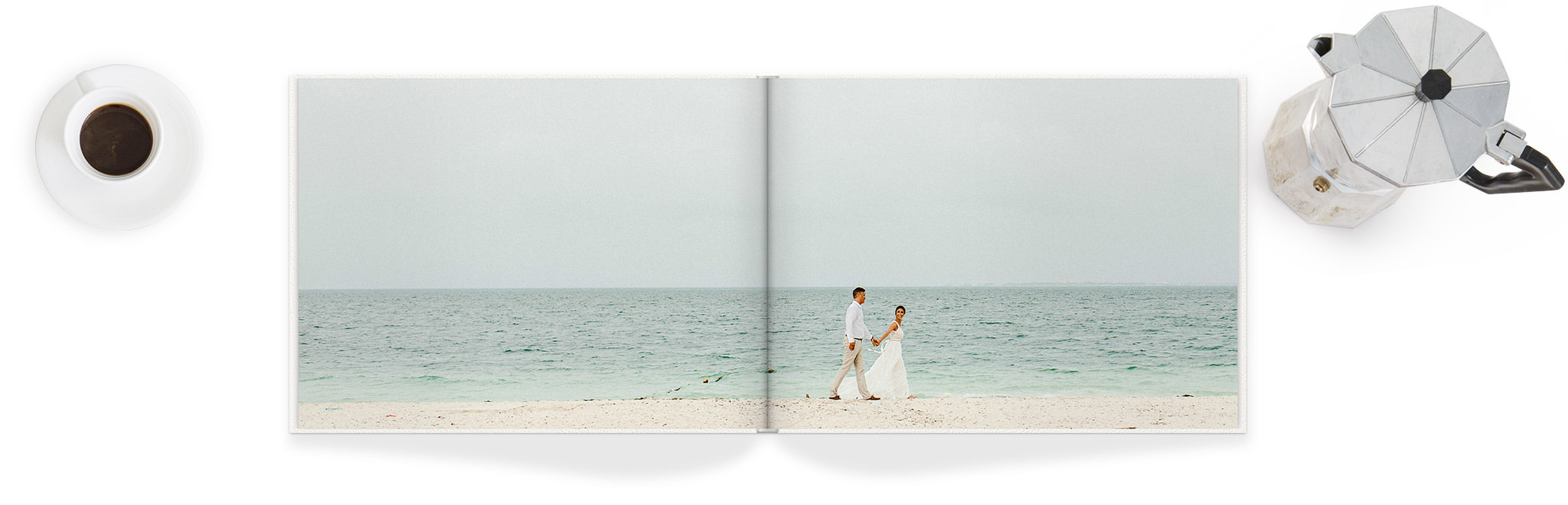 Fotolibro abierto con una doble página de una pareja de recién casados caminando de la mano por una playa.