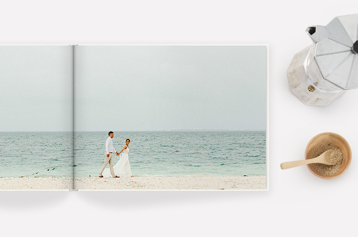 Libro fotografico aperto con una doppia pagina di una coppia di sposi che camminano mano nella mano su una spiaggia.