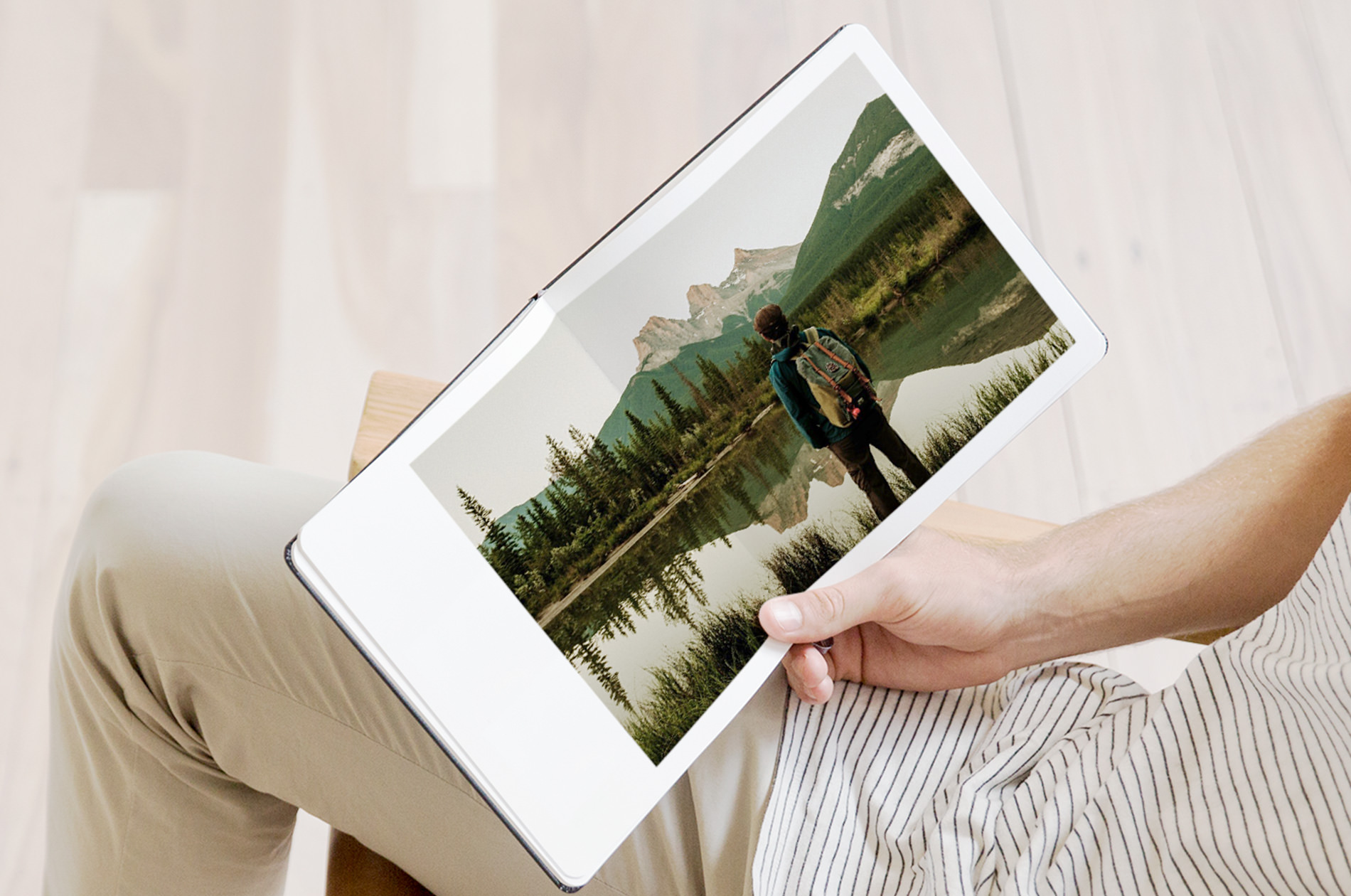 Male holding an open Moleskine Photo Book with an image of person overlooking a lake and forest landscape.