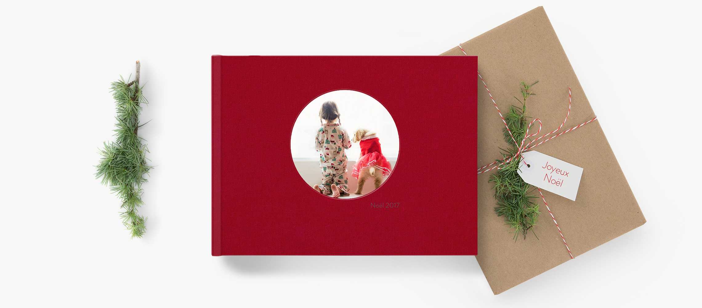 Un fotolibro rojo junto a un regalo de Navidad rodeado de adornos navideños.