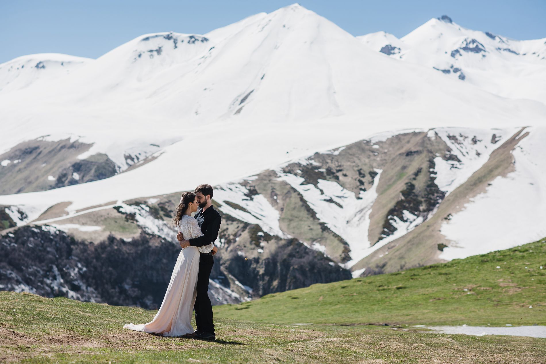 Bride in groom embrace at foot of mountains