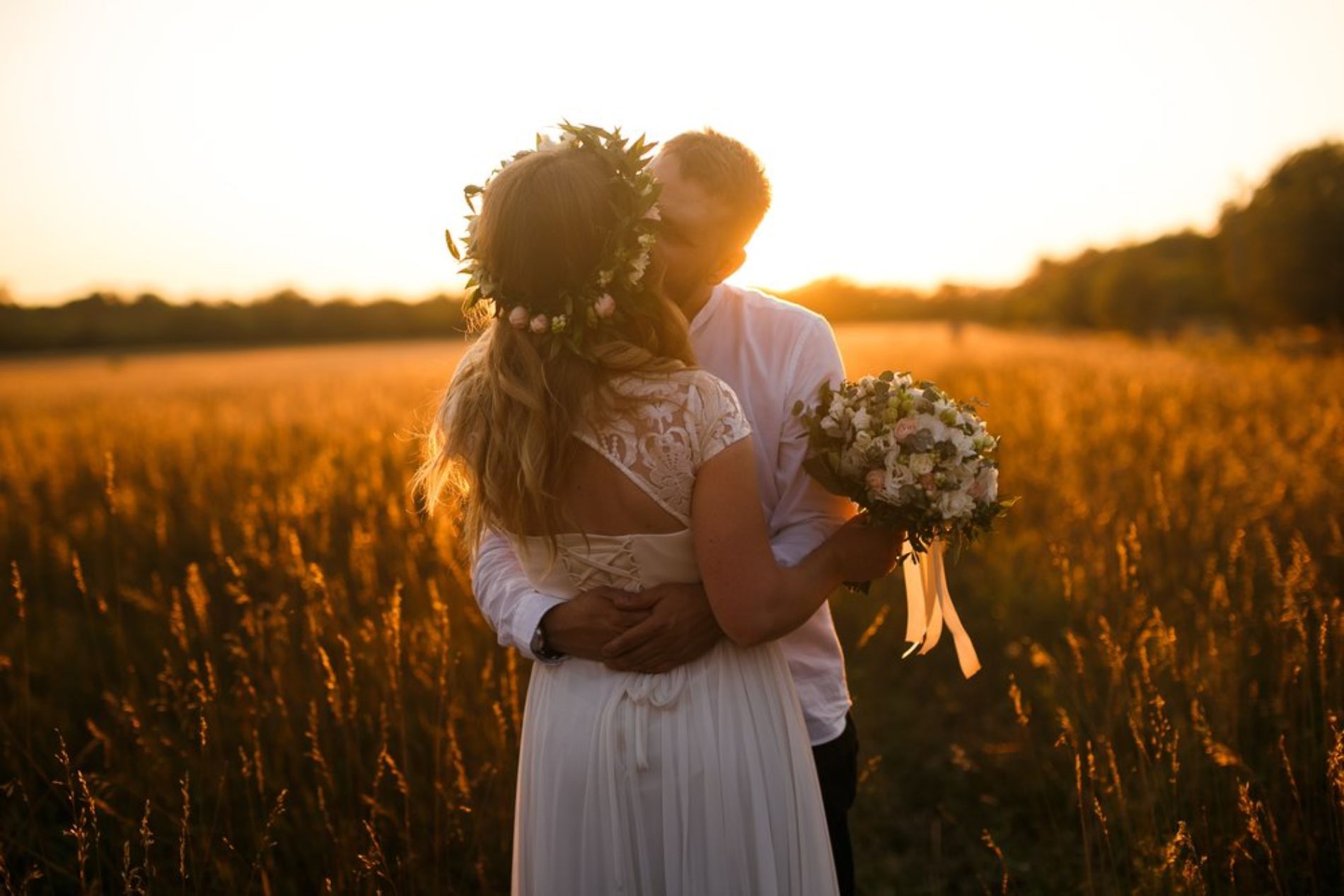 Newlyweds kiss in field at sunset