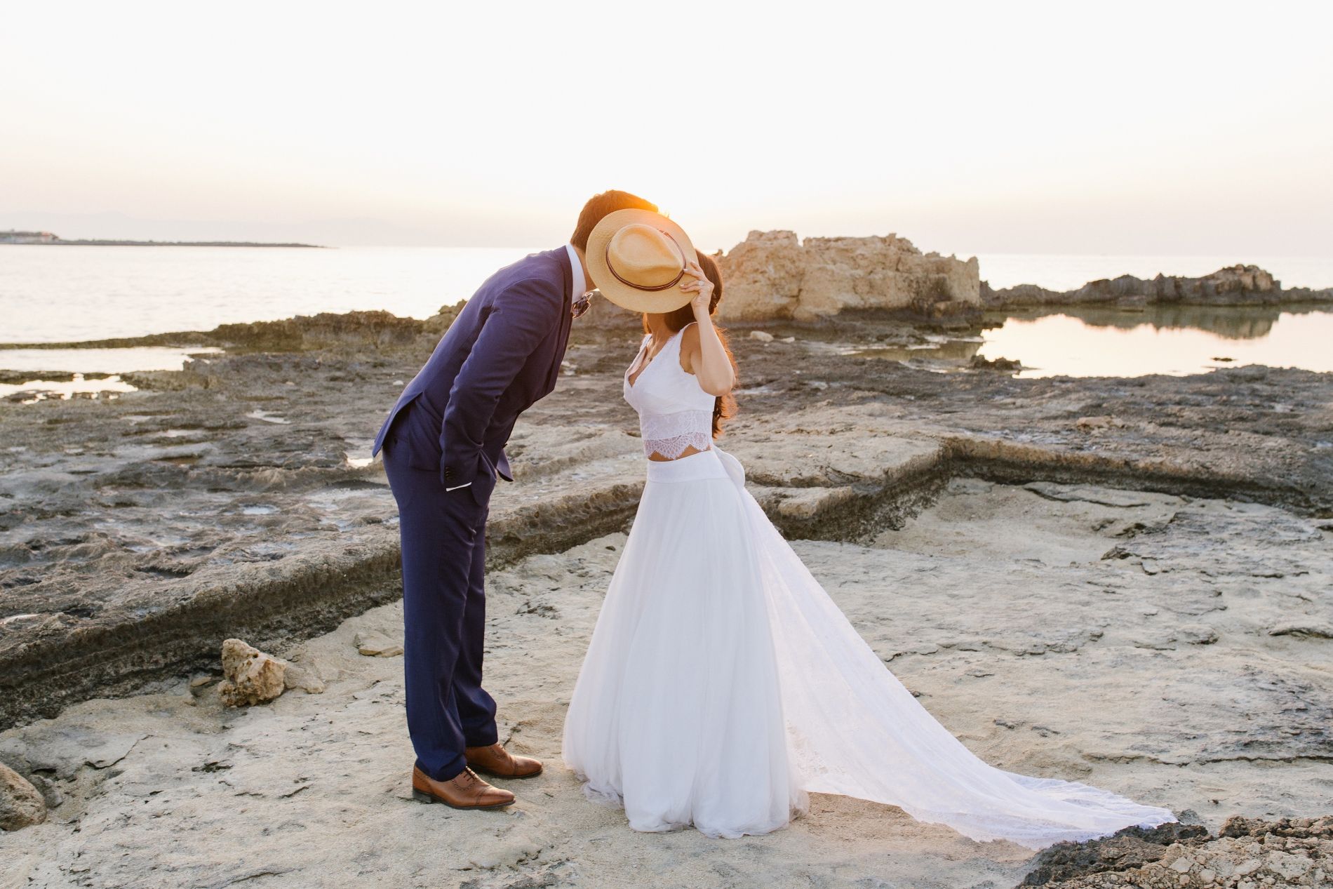 Newlyweds kiss behind hat by the sea