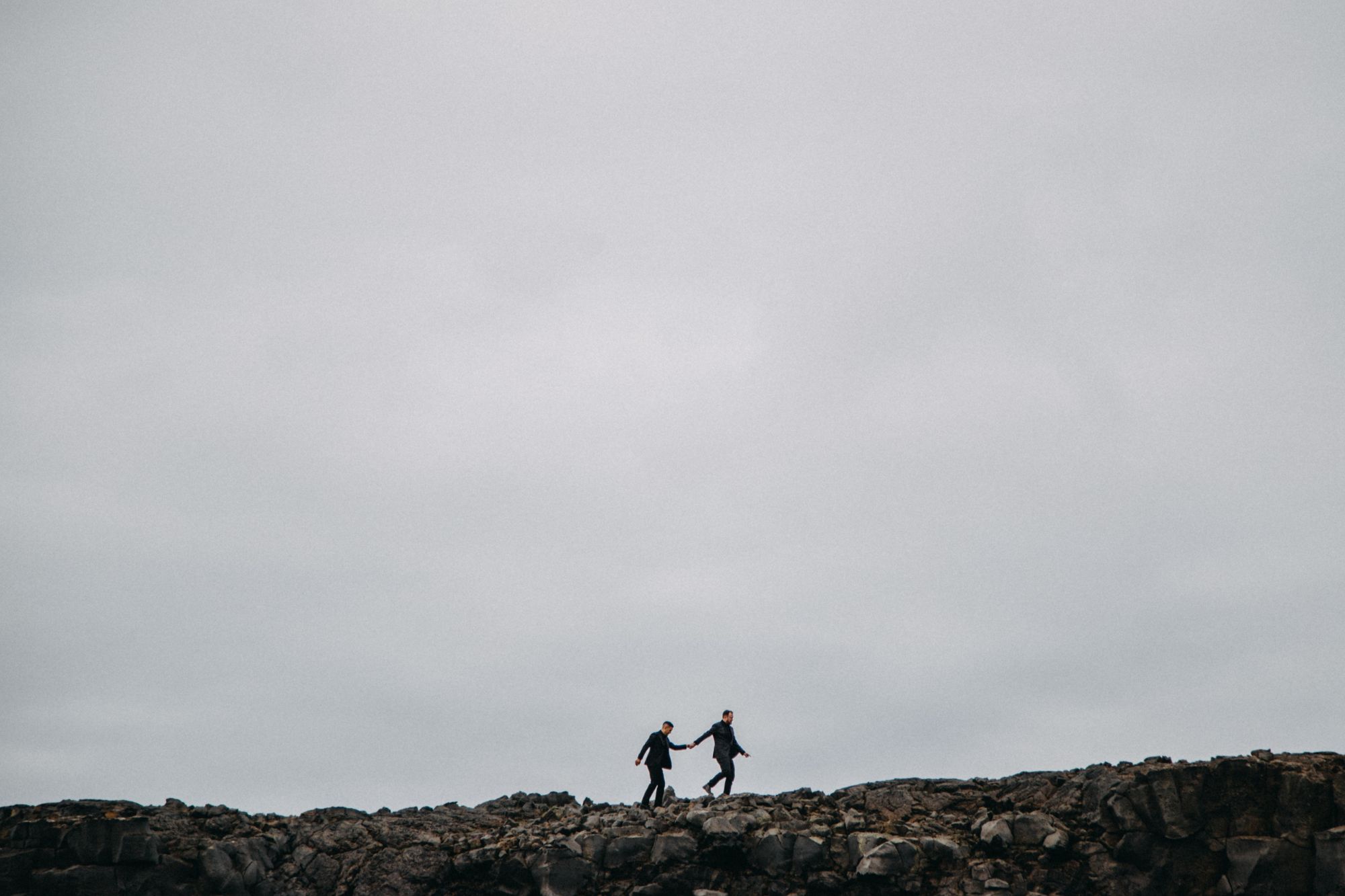Newlywed grooms walking across rocky Iceland landscape.