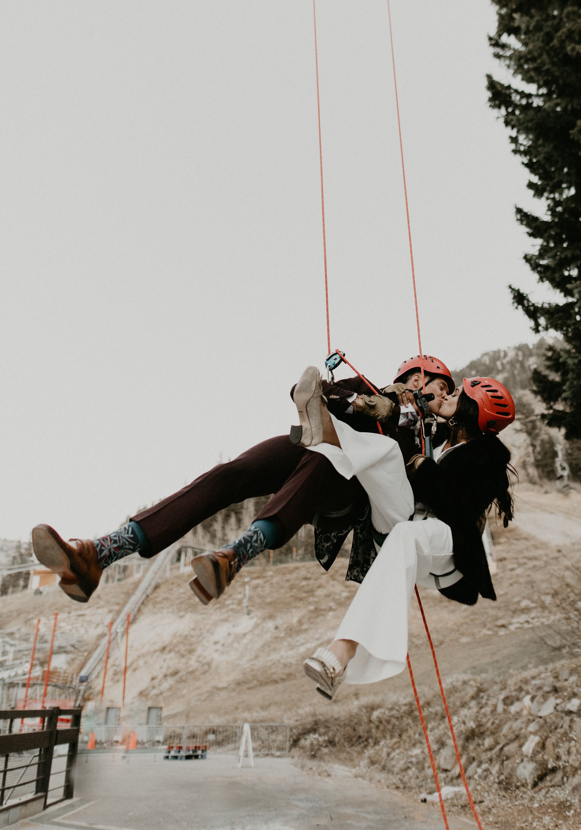 Newlywed couple wearing helmets, suspended in harnesses.